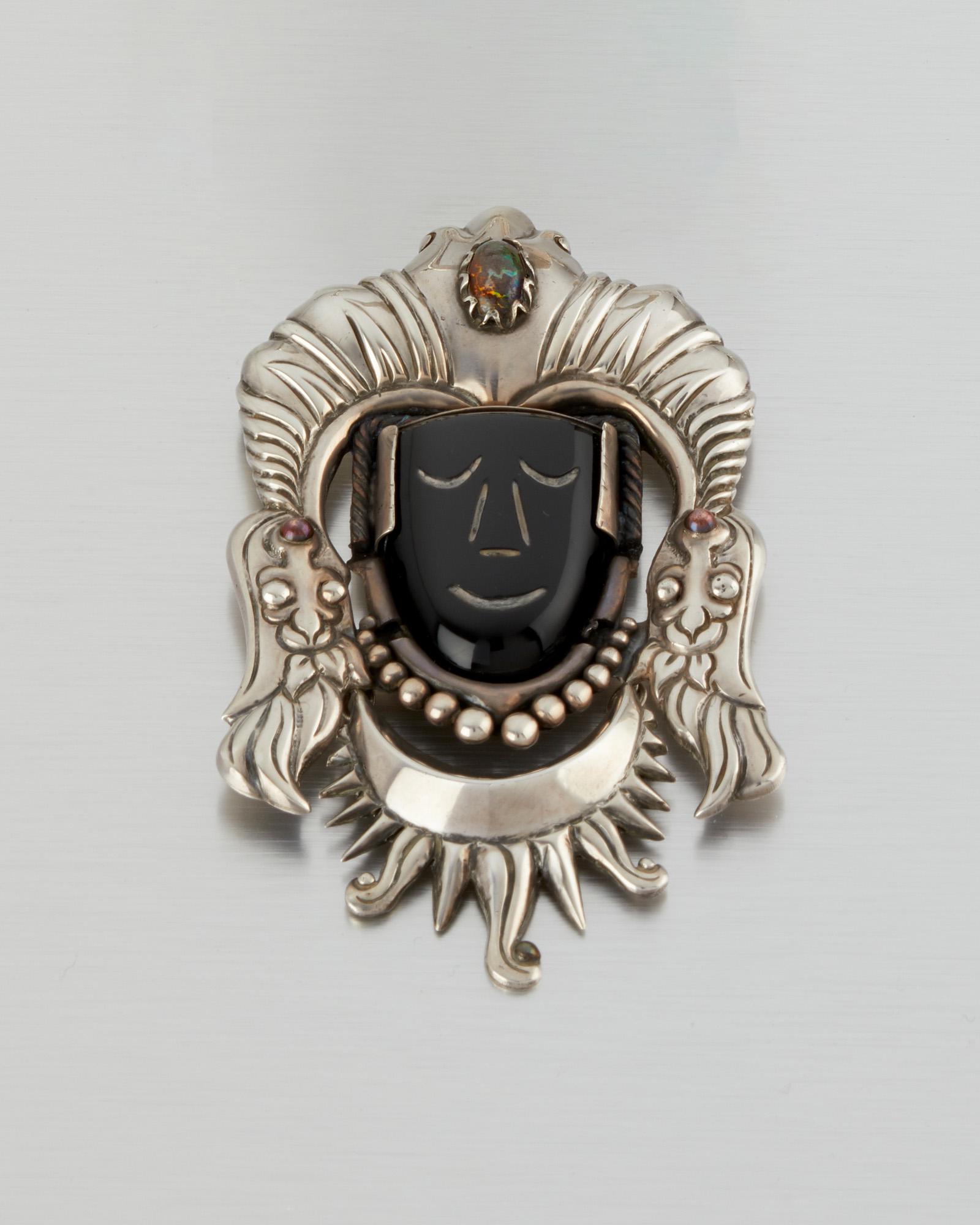 An Antonio Pineda silver and onyx brooch: 1948-1953; Taxco, Mexico Stamped: Silver by Tono: Further stamped: Mexico The carved onyx mask figure set into a silver brooch topped with an oval boulder opal head ornament with copper detailing 4.25
