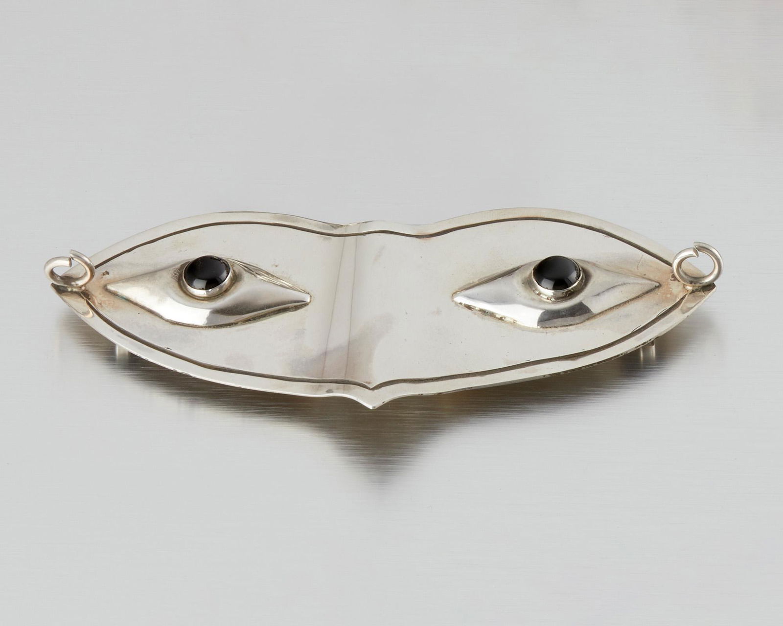 A Hubert Harmon sterling silver and onyx belt buckle: 1944-1948; Taxco, Mexico Winged feet for Hubert Harmon; Further stamped: Hubert Harmon / Sterling / Made in Mexico Designed as a masquerade mask set with cabochon onyx eyes 5.5" W x 2.25" H 91.5 g