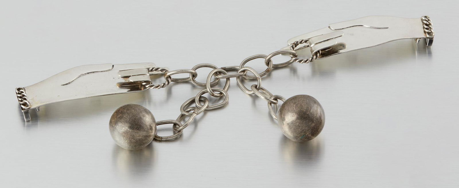 A Hubert Harmon silver and metal belt: 1944-1948; Taxco, Mexico Stamped for Hubert Harmon; Further stamped: Sterling / Made in Mexico Designed as two hands pulling a silver chain suspending two metal spheres on a black suede strap, 2 pie