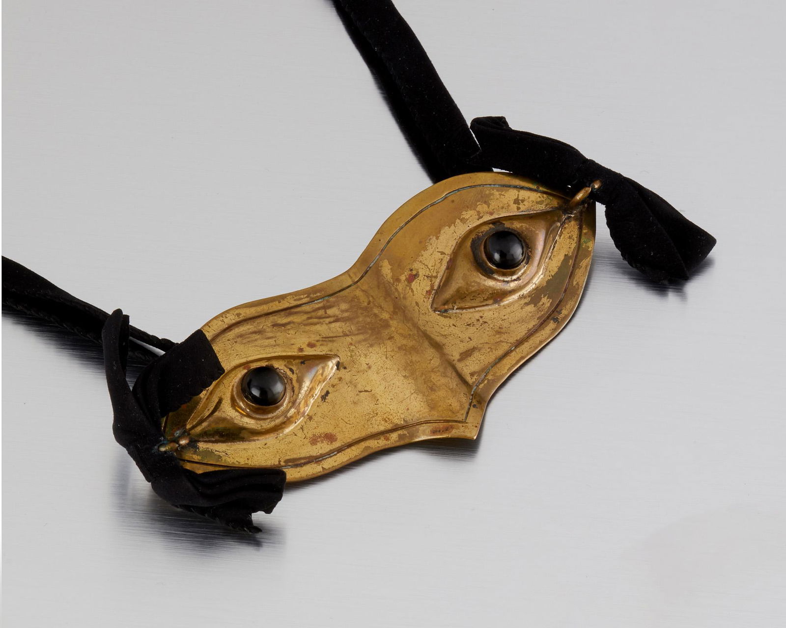 A Hubert Harmon brass and obsidian mask belt: 1942-1948; Taxco, Mexico Stamped for Hubert Harmon; Further stamped: Mexico The masquerade mask belt set with obsidian cabochon eyes on a double-strand velvet cord Buckle: 5.5" W x 2" H 66.0 grams