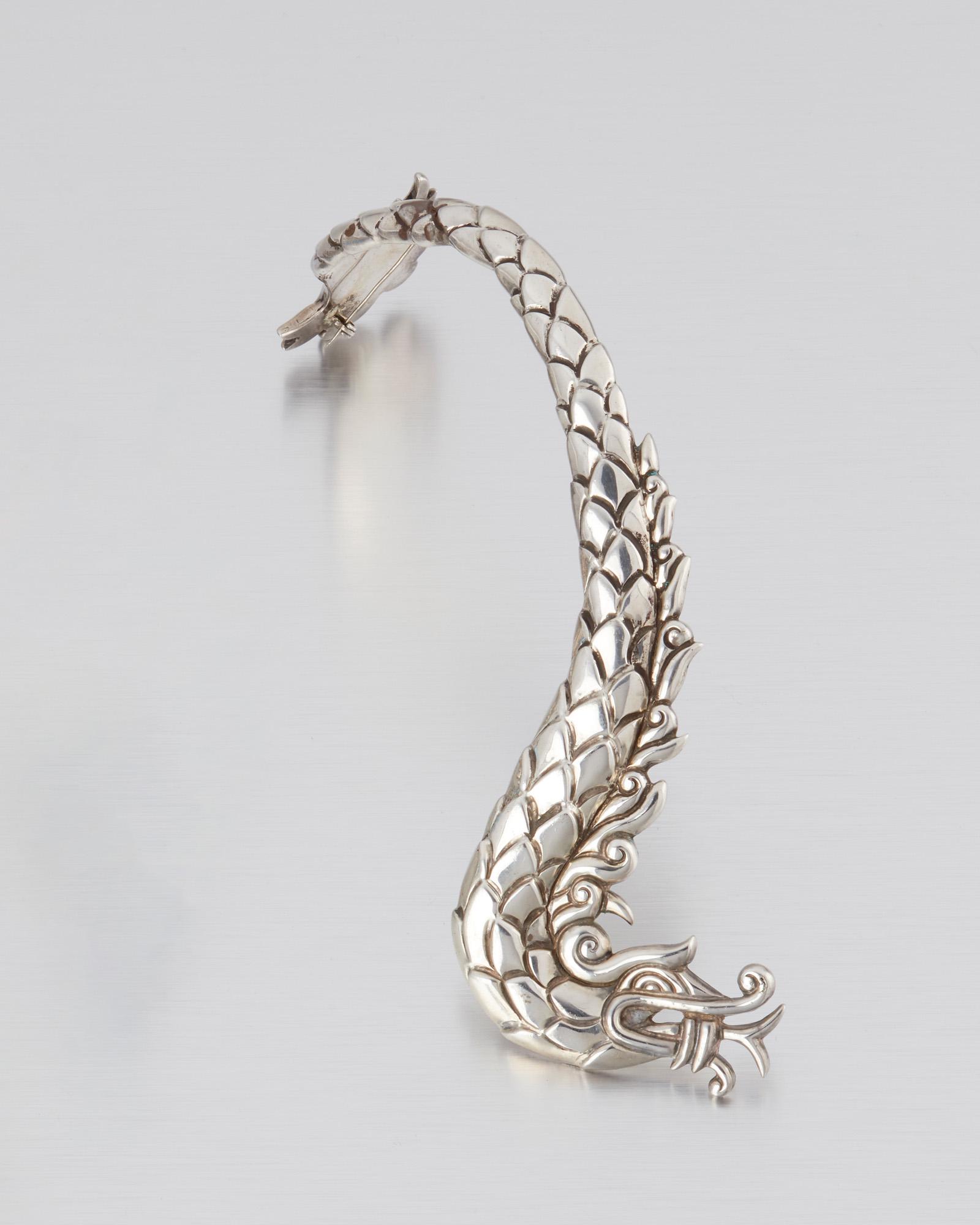 A Los Castillo sterling silver dragon shoulder brooch: 1939-1945; Taxco, Mexico Stamped: Los Castillo; Further stamped: Taxco / Sterling / Made in Mexico The repousse dragon-motif brooch designed with two brooch backings to be worn from the shoulder to th