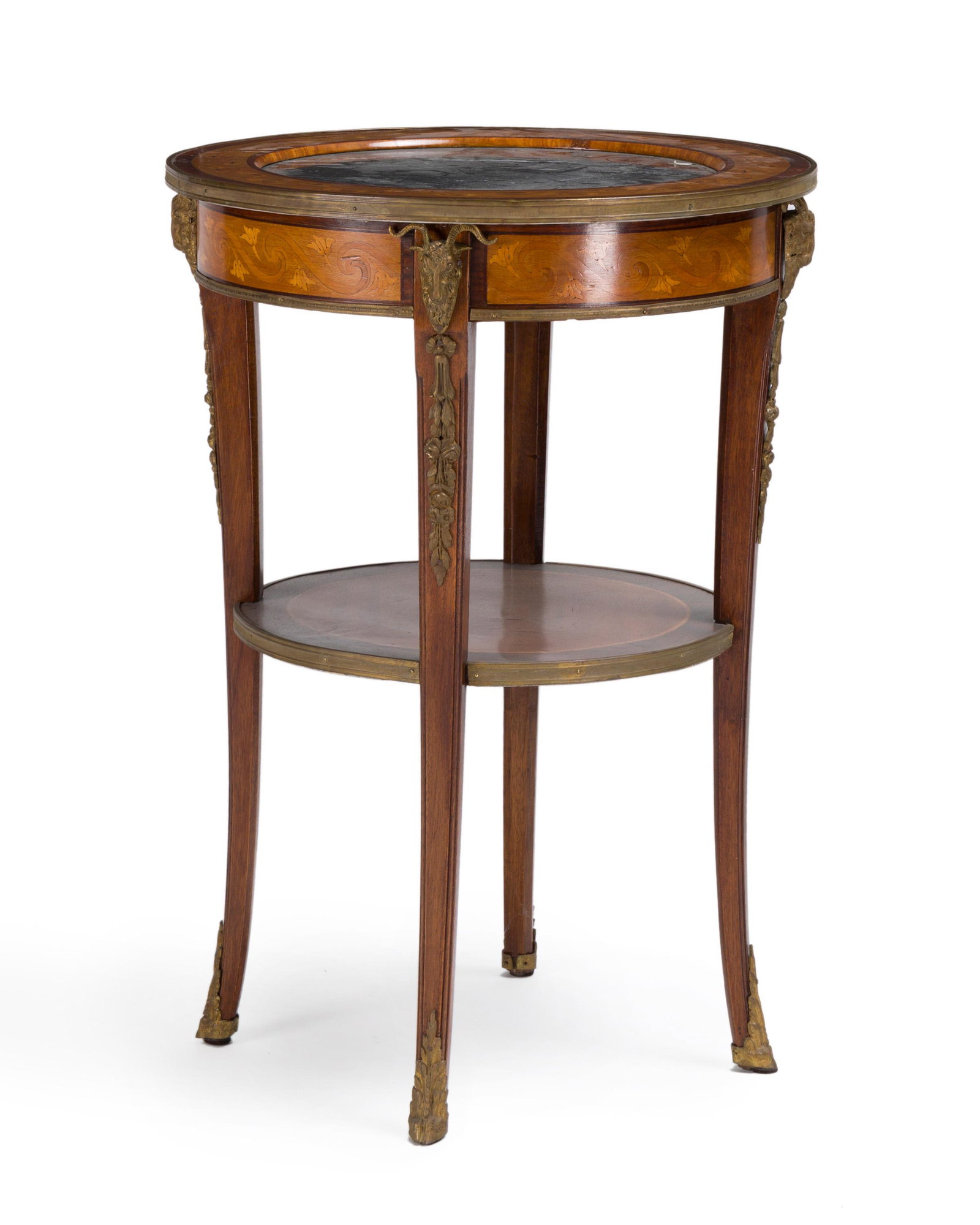 A French gueridon table with marble top: First quarter 20th century The inset black marble top enclosed in a marquetry wood frame over a marquetry apron raised on slightly outswept legs adorned with gilt bronze ram's head masks raised on hoo