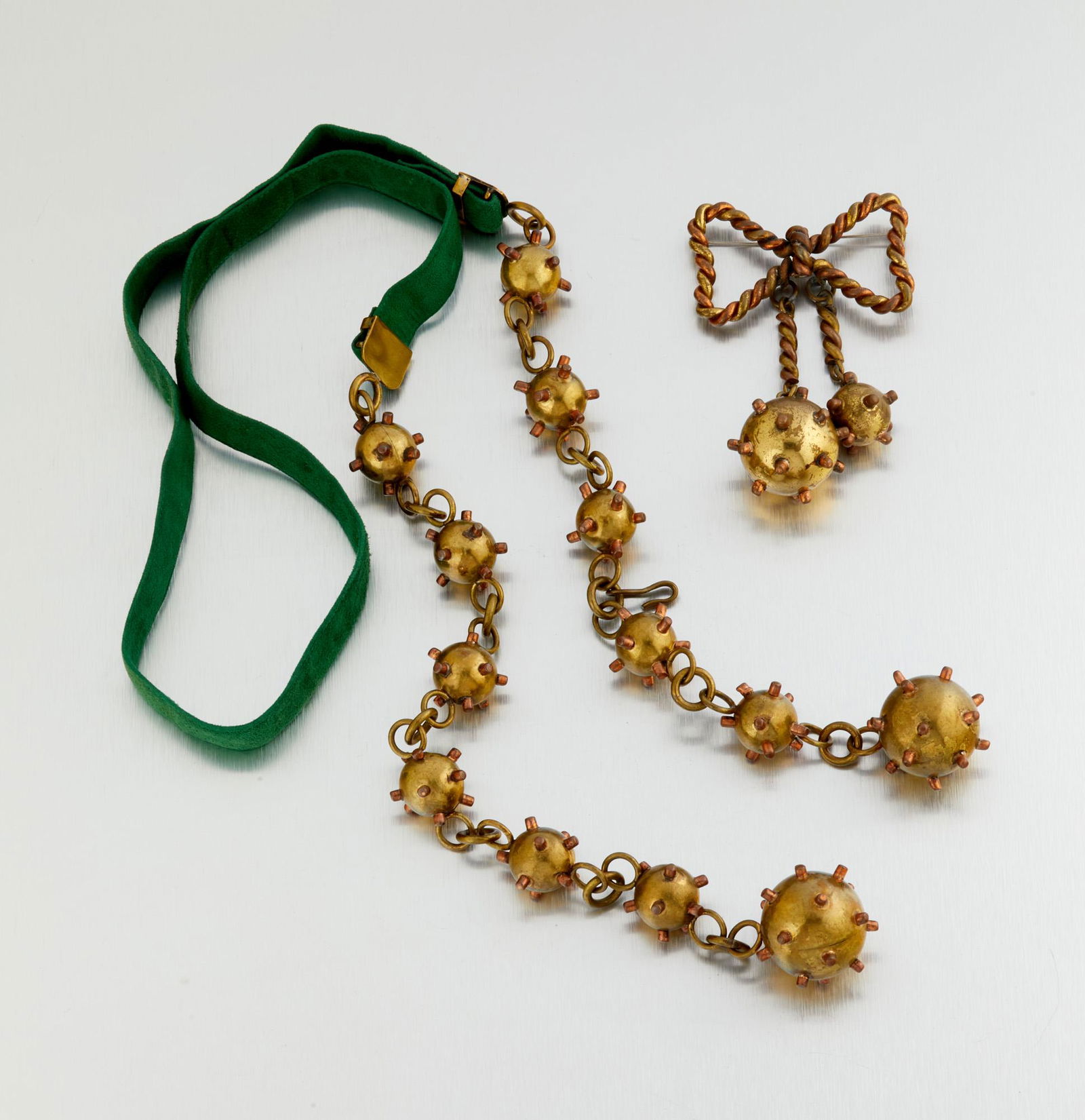 Two Hubert Harmon mixed-metal jewelry items: 1944-1948; Taxco, Mexico Stamped for Hubert Harmon; Further stamped: Mexico Each with copper appendages on brass, comprising a belt designed with stylized bombs on an adjustable green leather belt (
