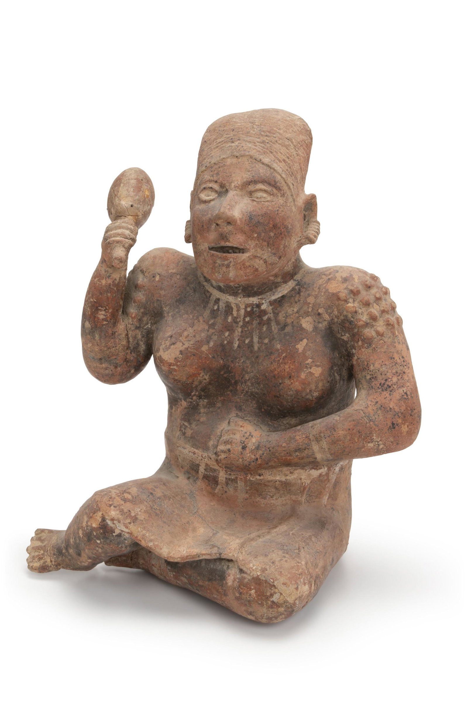 A Pre-Columbian terracotta figure: Circa 250 BCE-250 CE; Jalisco, Itzalan (West Mexico) The seated female earthenware figure with ear, arm, and neck ornaments wearing a cap and knee-length skirt and holding a large rattle, bumps on her