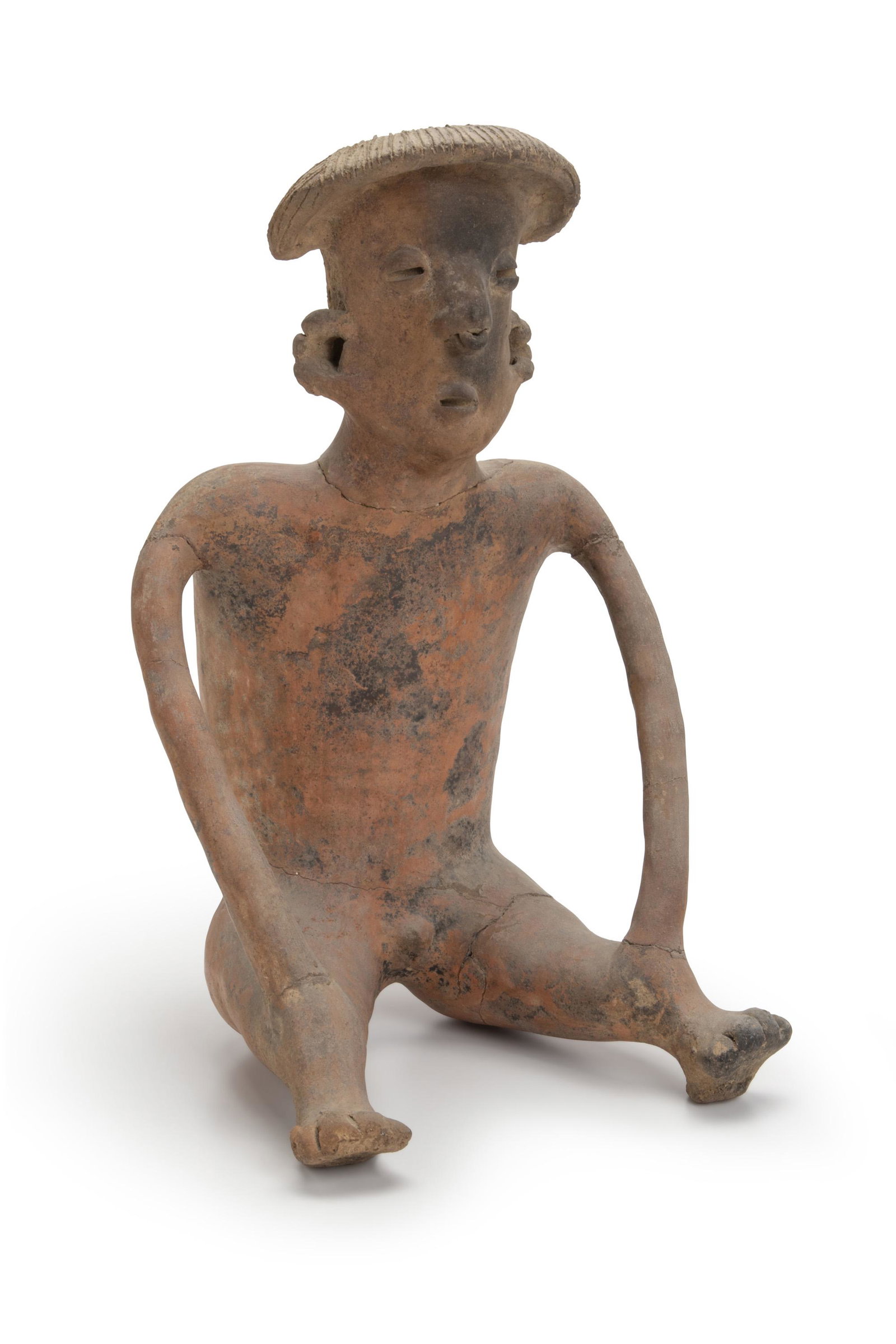 A Pre-Columbian terracotta figure: Circa 250 BCE-250 CE; Nayarit (West Mexico) The seated male earthenware figure with matted coiffeur in a hooded style, long face, ear and nose ornaments, and typical "coffee bean" eyes with long thin 