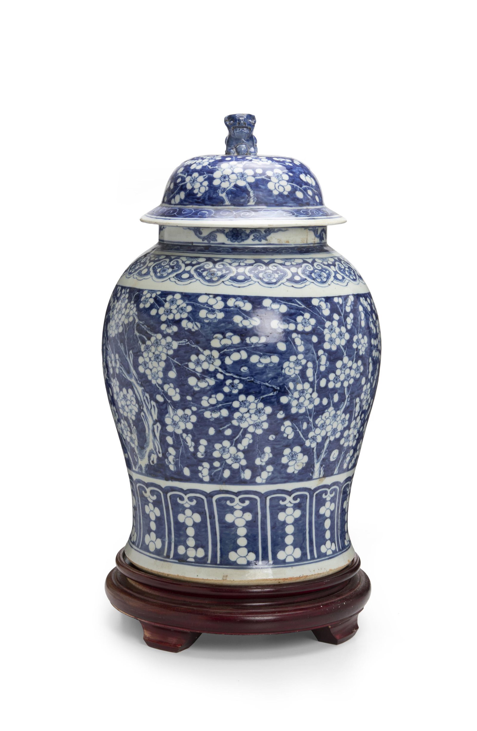 A tall Chinese blue and white lidded vase: 20th century Unmarked The large baluster-shaped vase on a footed wood stand with blue painted cherry blossom motif and lid with lion handle 26.5" H x 13.5" Dia.