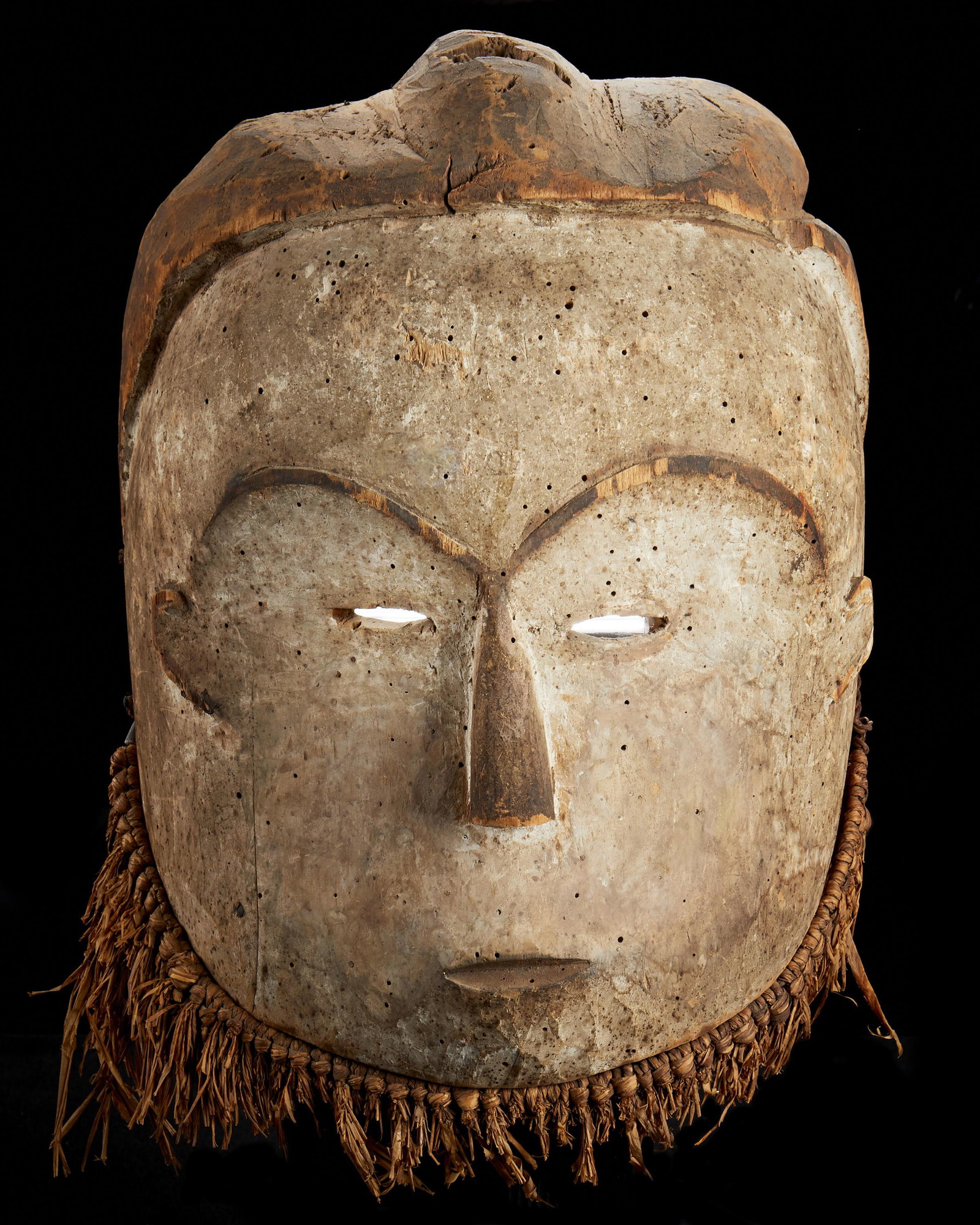 A ritual Fang mask: Late-19th Century; Fang culture, Gabon The carved wood mask in ovoid shape with arched eyebrows and slit eyes, woven grass fibers attached to bottom edge 11" H x 8.5" W x 4" D Provenance: Collection o