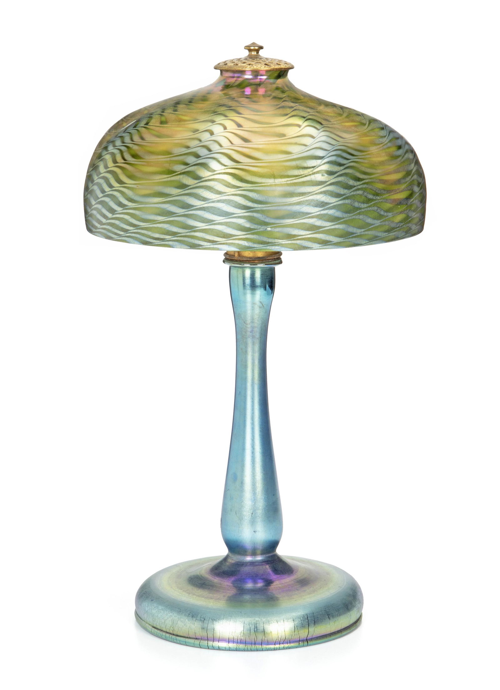 A Tiffany Studios iridescent and Favrile glass table: Late 19th/early 20th century Shade signed to fitter rim: L.C.T.; Base signed: L.C. Tiffany - Favrile; Socket stamped: Hubbell 125 V The blue damascene shade with white interior over a single gilt-bron
