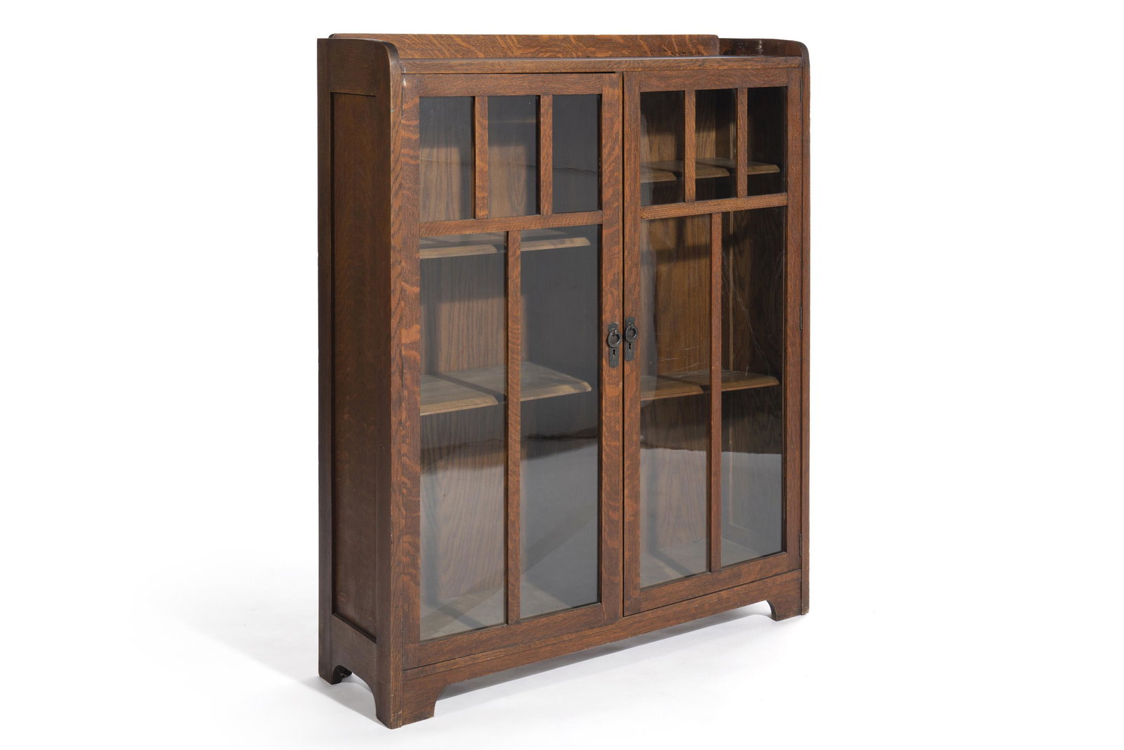 An Arts & Crafts double-door bookcase: First-quarter 20th Century Two single glass pane doors each divided into five-lights by a wood frame enclosing four adjustable shelves 54.5" H x 44.75" W x 13" D