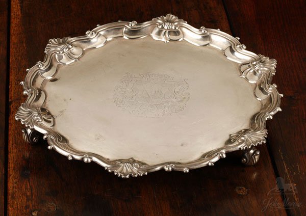 A George II sterling silver footed salver: 1759, London, with maker's mark ''JM'', possibly Jason Morrison, the waved circular rim decorated with C-scrolls and ruffled shells, centering a heraldic crest featuring a triple-masted ship and a tri