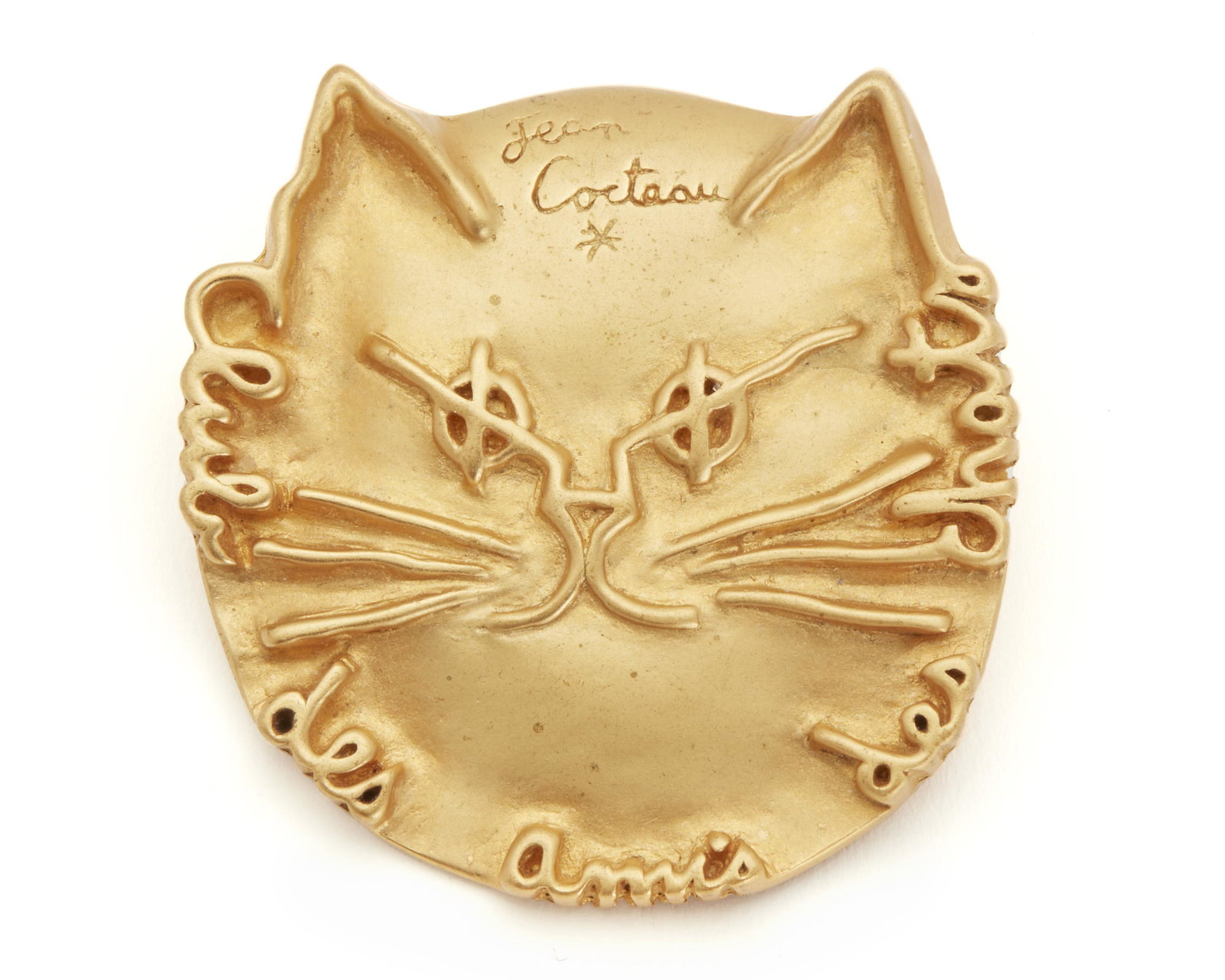 An After Jean Cocteau cat brooch: Signed: Madeline Flammarion / Comite Jean Cocteau / 1999 Gilt bronze in the form of a cat head and inscribed: Jean Cocteau / club des amis des chats 1.5" H x 1.5" W