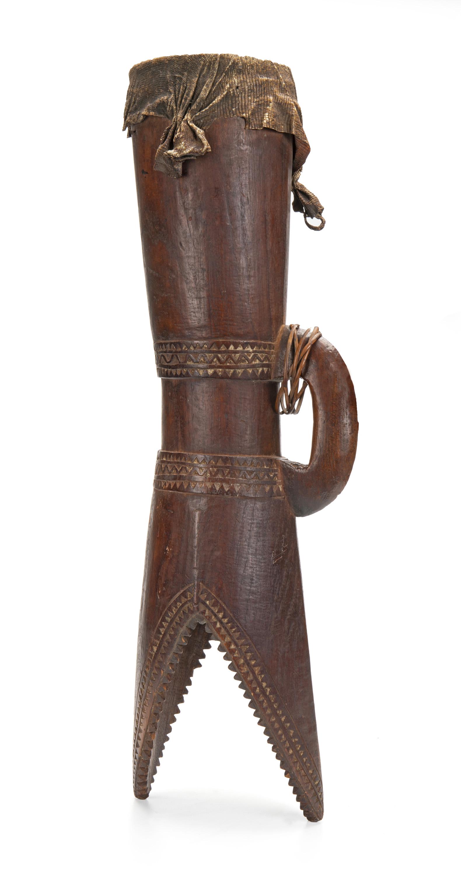 A Papua New Guinea "Kundu" hand drum: 20th Century; Papuan Gulf The hardwood drum with traces of white lime to the carved patterning and in the form of a stylized open-mouthed crocodile with handle 29" H x 8" W x 6" D