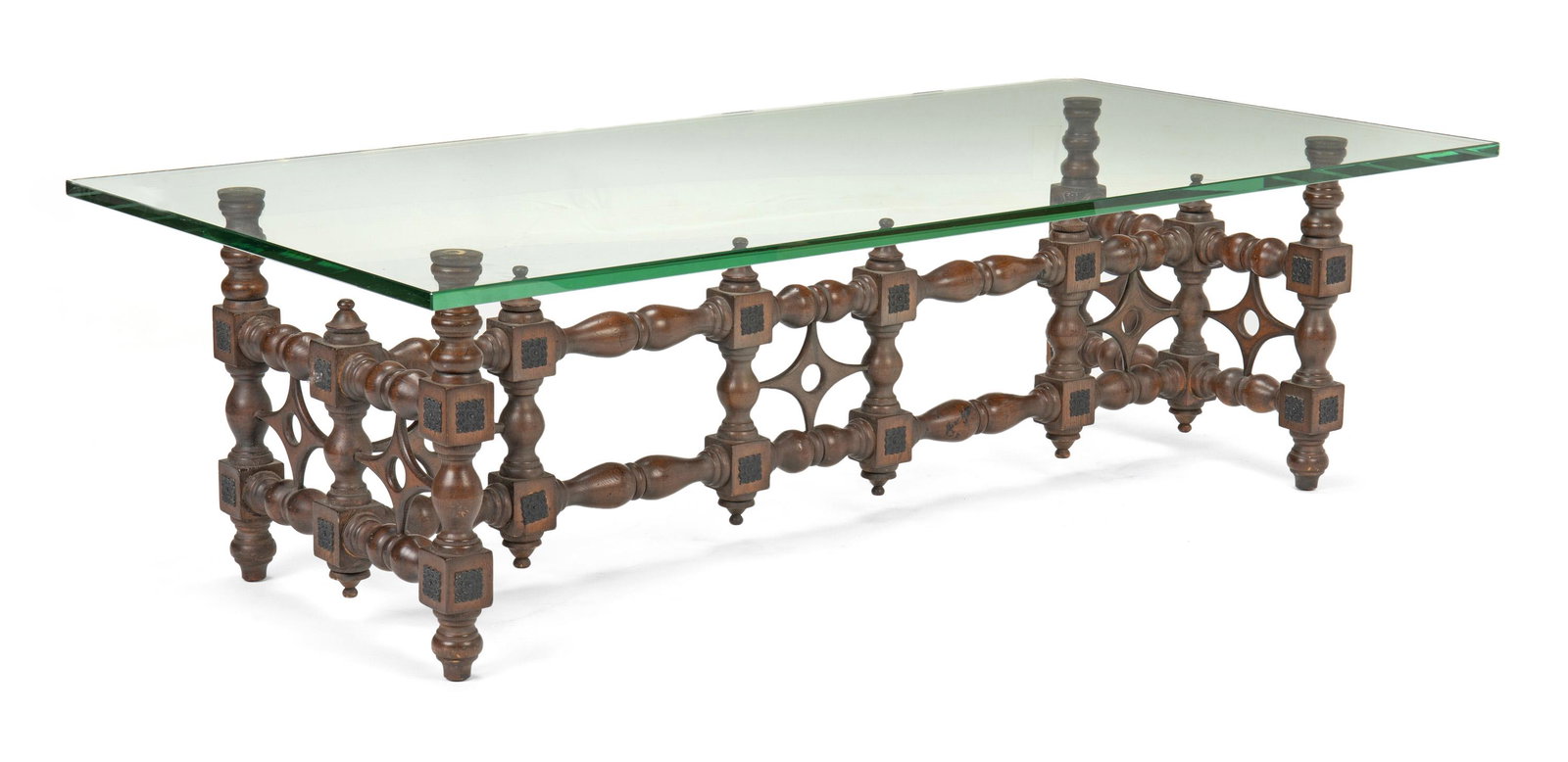 A Moroccan-style rectangular carved wood cocktail table: Circa 1960 The rectangular table with glass top resting on turned wood body with carved diamond decorated stretcher and ornamental metal medallions 17.5" H x 59" W x 30" D