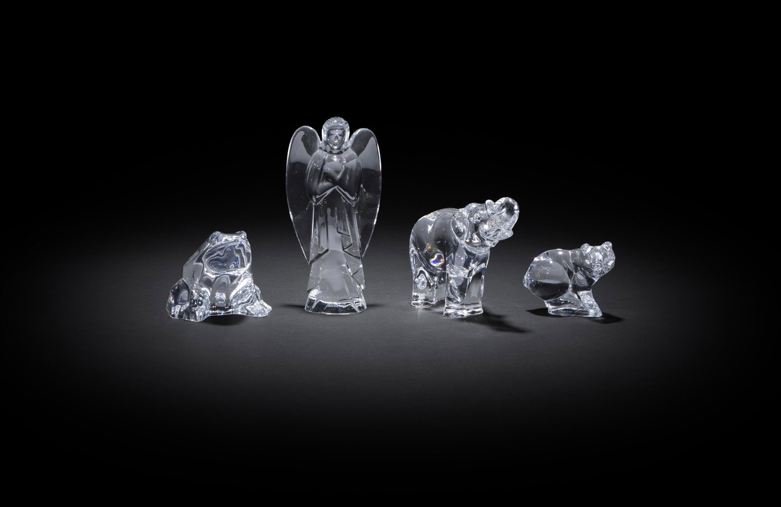 Four clear art glass figures: Fourth-quarter 20th Century Each marked for maker Comprising a Baccarat angel, a Baccarat frog, a Baccarat elephant, and a Daum pig, 4 pieces Largest: 6" H x 3" W x 1.625" D