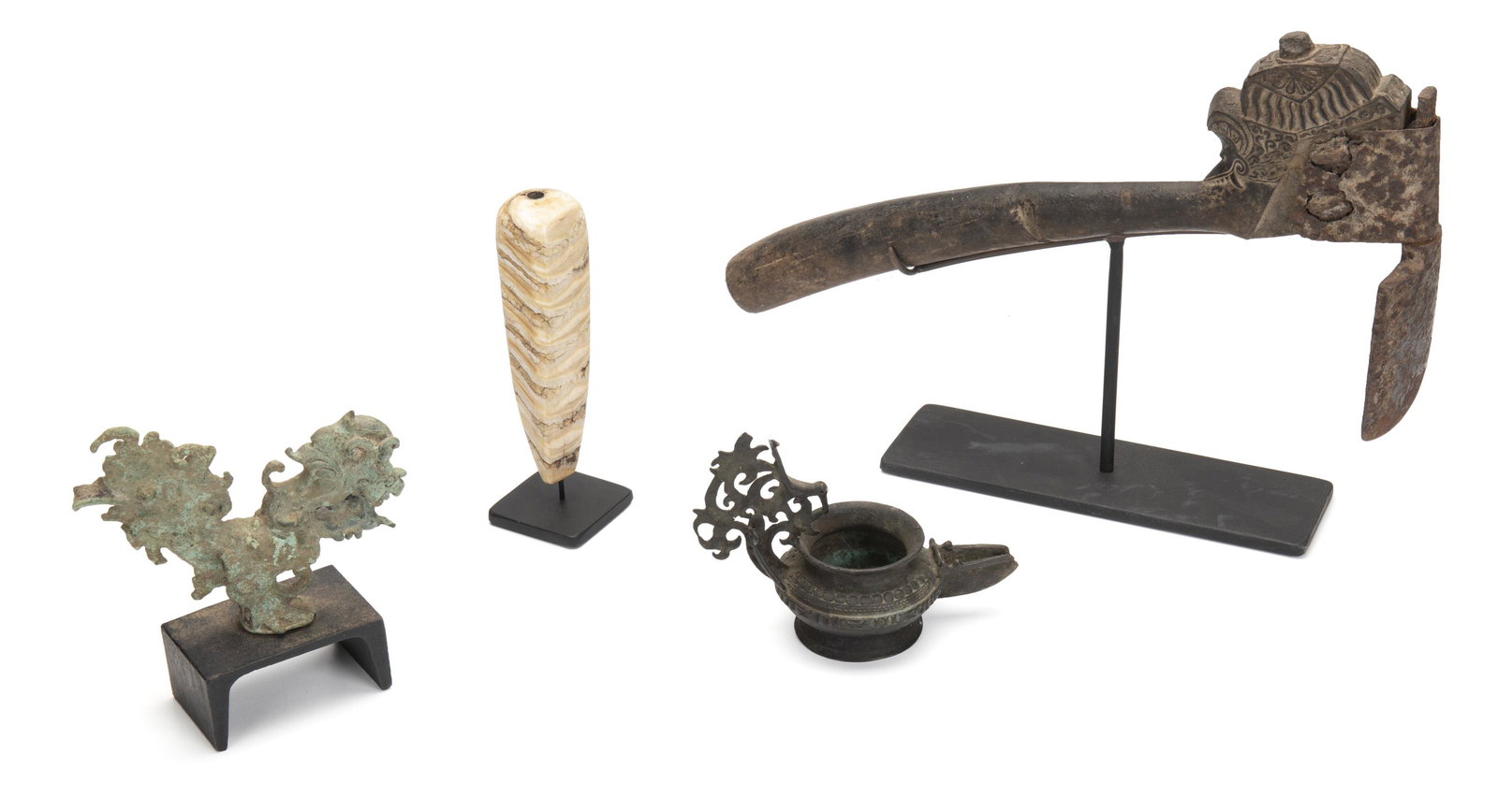 Four Indonesian items: 20th Century and earlier Comprising an adze with an ornamented carved handle, a banded stone cigarette holder, a bronze lamp with a reticulated handle, and a zoomorphic bronze finial in the form of a 