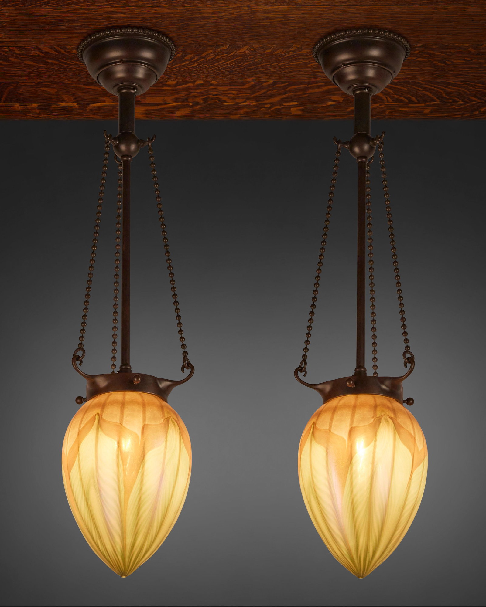 A pair of L.C. Tiffany Favrile glass pendant lights: First-quarter 20th Century; New York, NY Shades signed: L.C.T. Each teardrop-shaped gold iridescent Favrile glass shade with green pulled feather motif fitted with an associated single-light patinated
