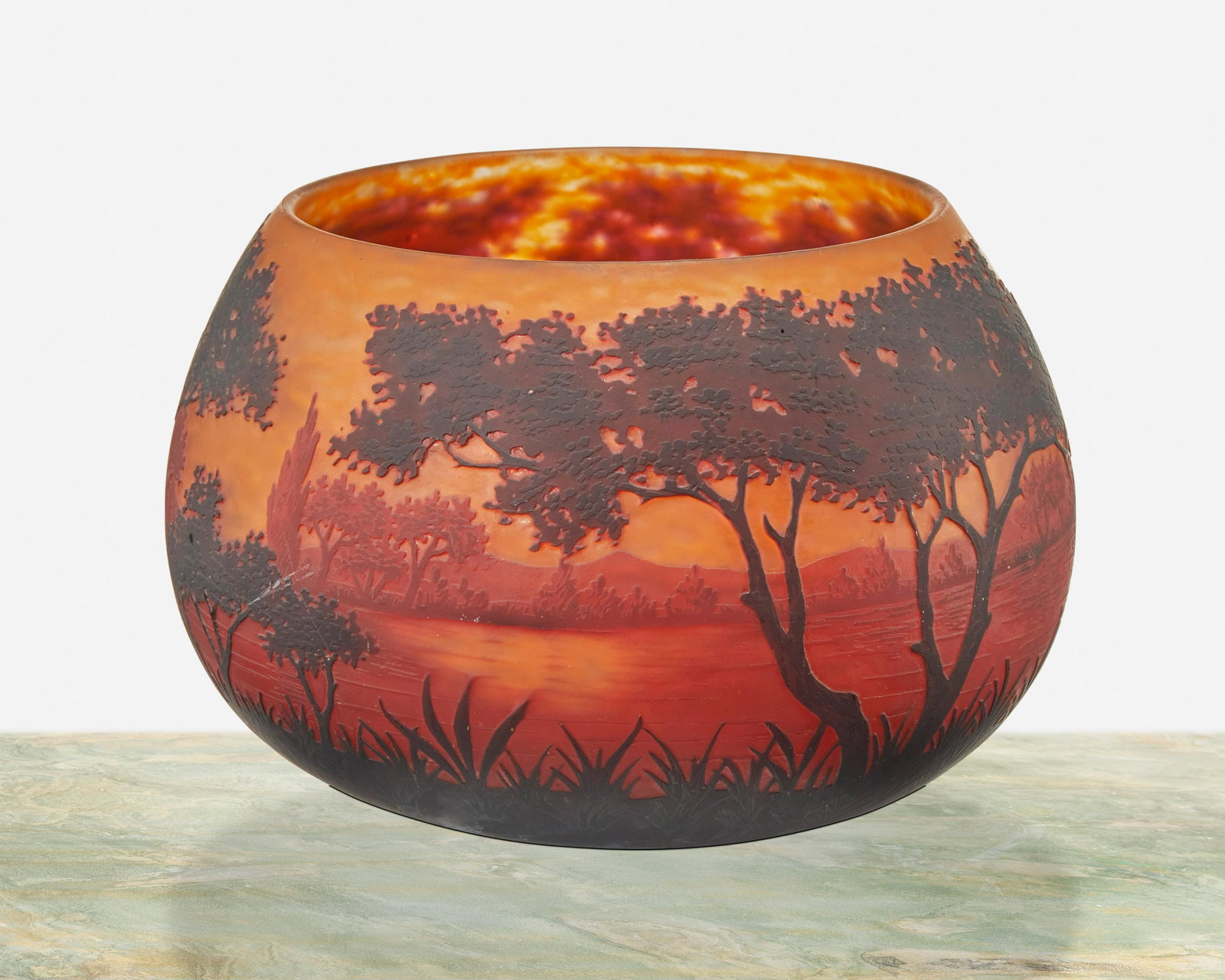 A Daum cameo glass "Paysage du Lac" bowl: First-quarter 20th Century; Nancy, France Signed: Daum Nancy [Croix de Lorraine] The acid-etched cameo glass bowl cut from dark red and red to orange frost with wooded lakeside motif 5.5" H x 8" Dia. 