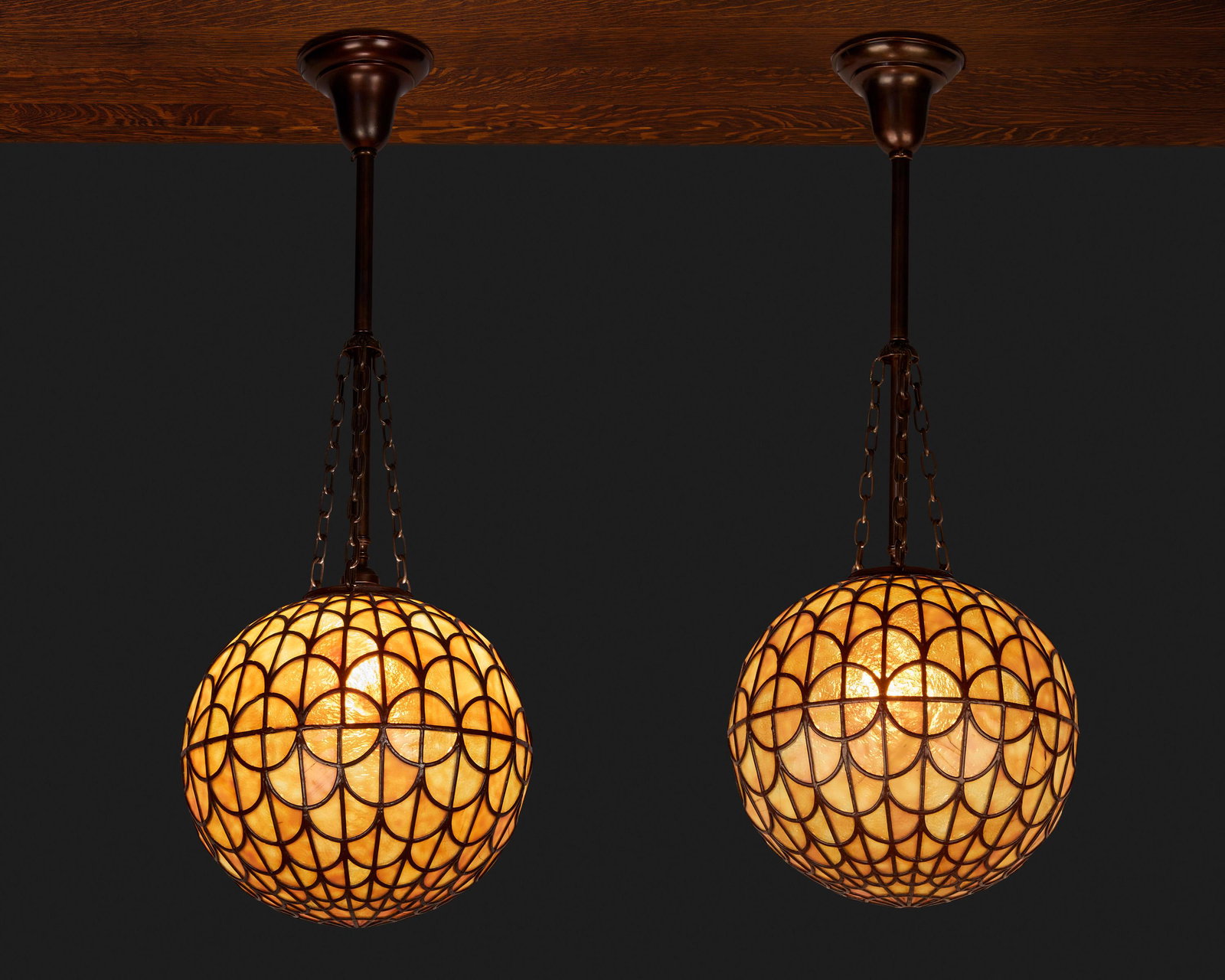 A pair of spherical leaded glass pendant chandeliers: Circa 1900-1910 Each caramel-colored pendant chandelier of painted lead came construction with fish scale pattern fitted with a single light socket and patinated metal stem, canopy, and suspended chai