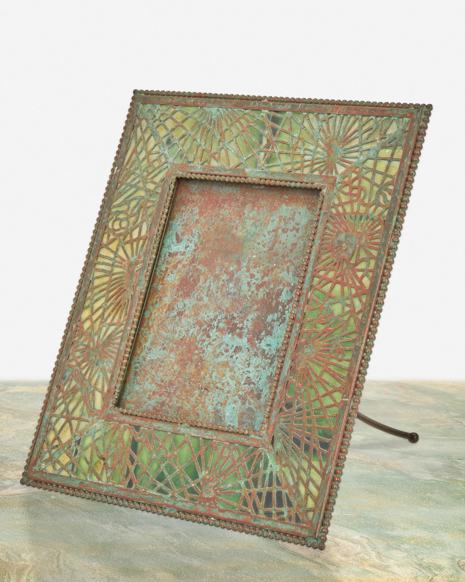 A Tiffany Studios bronze pine needle frame: Circa 1902-1919; New York, NY Signed: Tiffany Studios / New York / 947 The rectangular verdigris patinated bronze frame with green glass, pine needle motif bronze overlay, and beaded border enclosing 