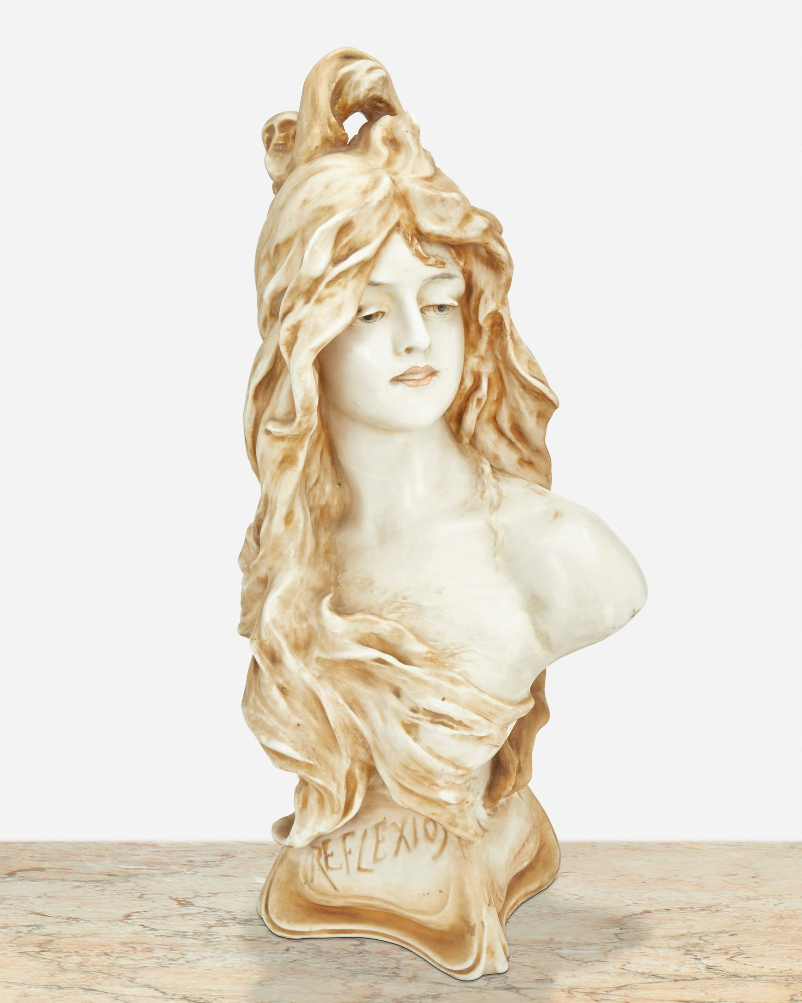 An Amphora "Reflexion" ceramic bust: Late 19th/early 20th Century Marked: Amphora / 1243 / 21 The ceramic bust depicting a woman with flowing hair atop a squared plinth inscribed "Reflexion" 20" H x 10.5" W x 8" D Provenance: The Alan Sc