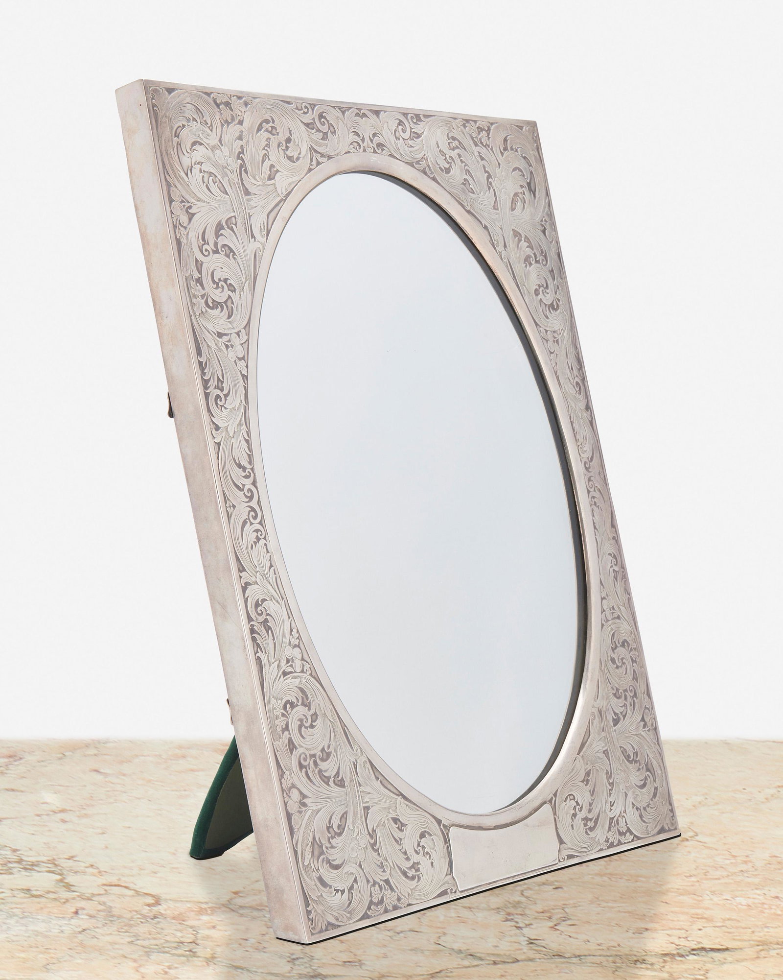 An American sterling silver framed table mirror: First-half 20th Century Marked for William B. Kerr & Co.; Further marked: Sterling / 3481 The rectangular sterling silver easel-back frame with scrolling foliate motif and cartouche to bottom enclosin