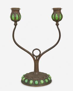 A Tiffany Studios double-arm bronze candlestick: Circa 1900-1902; New York, NY Signed: Tiffany Studios / New York / [T.G.D.Co. monogram] The patinated bronze candlestick with floral motif base and inset green Favrile glass cabochons issuing