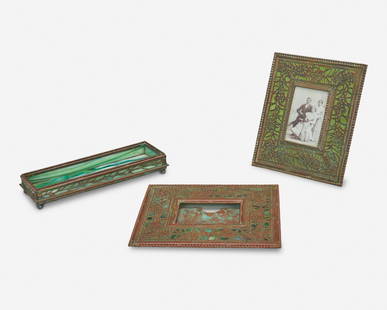 Three Tiffany Studios desk accessories: Circa 1902-1919 Each signed: Tiffany Studios / New York Each verdigris patinated bronze, comprising a rectangular picture frame with green rippled glass and foliate motif bronze overlay, a