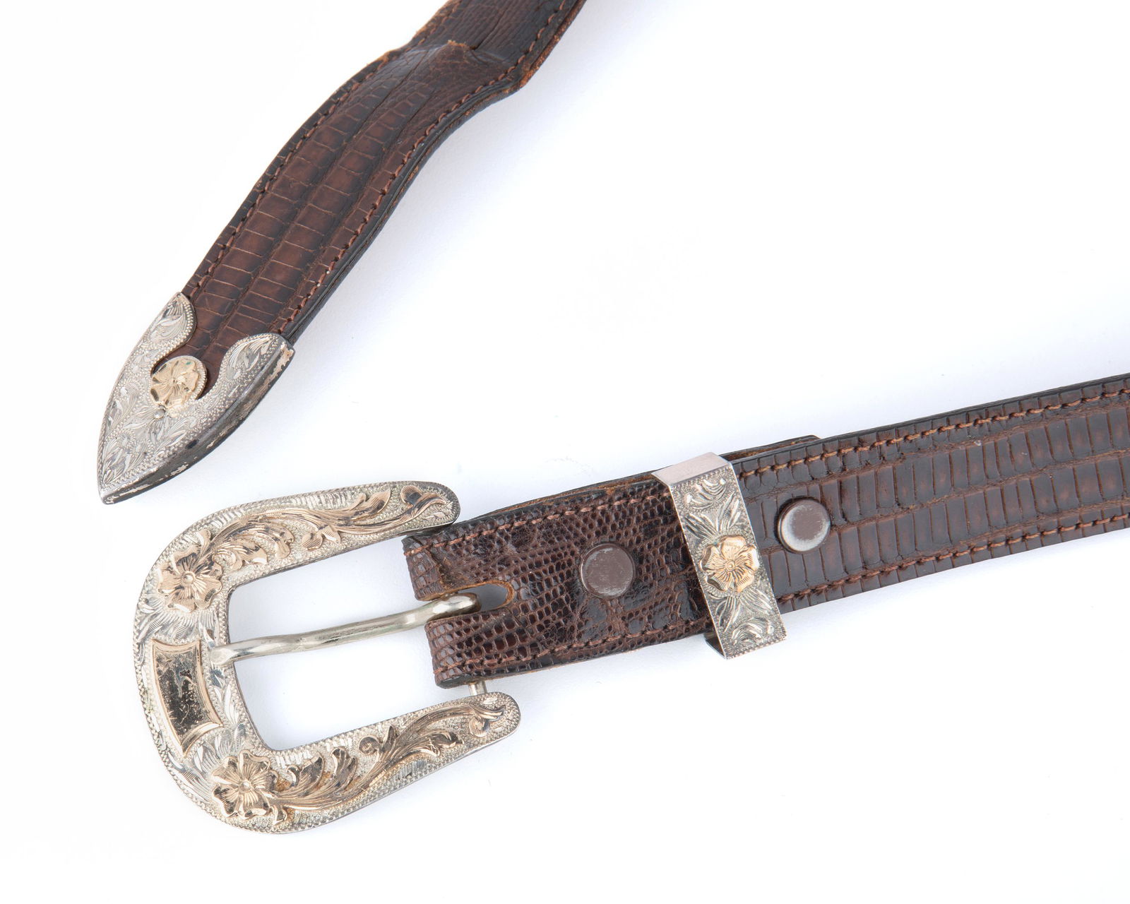 A Nudie's Rodeo Tailors Inc. 10k and sterling buckle: Stamped: Nudie's / Rodeo Taylors Inc. / 10k / sterling The sterling buckle and tip topped with 10k yellow gold are highly chased with floral pattern Buckle: 2" L x 1.8" W; Leather length: 36" Prov