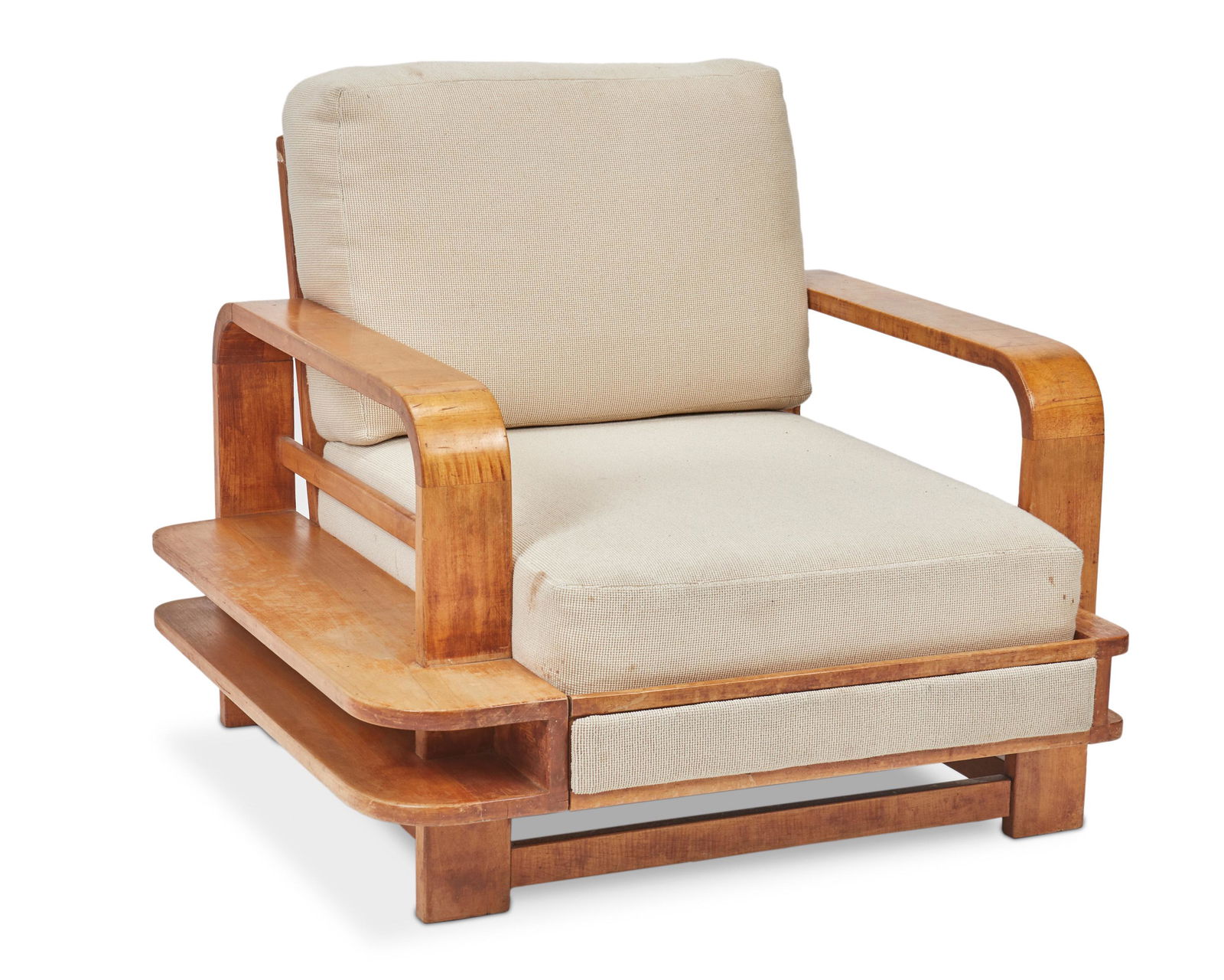 A lounge chair designed by Russel Wright for: Circa 1935 Appears unmarked The armchair with streamline asymmetrical wooden frame with rounded arms and fitted with beige upholstered seat and back cushions 31" H x 35" W x 35" D Provenance: Fro