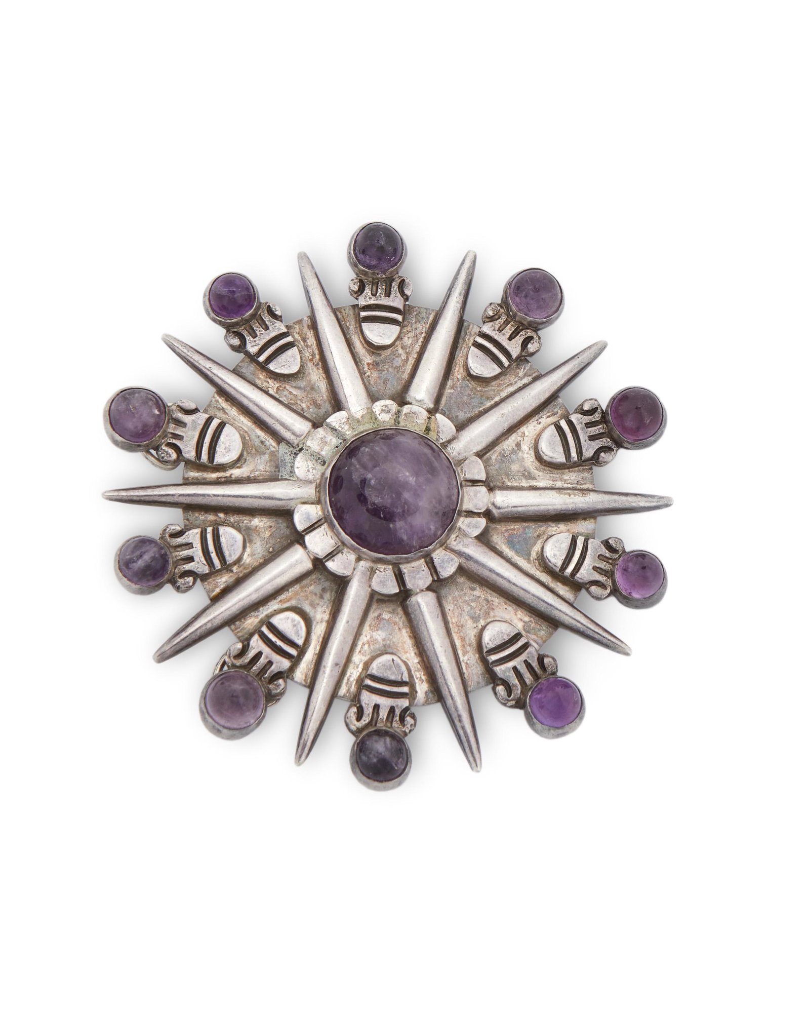 A William Spratling silver and amethyst pendant/brooch: Circa 1940-1946, First Design Period; Taxco, Mexico Stamped for William Spratling; Further stamped: Made in Mexico / Silver Designed as an Aztec sunburst inset with eleven cabochon amethyst 3" Dia. 82