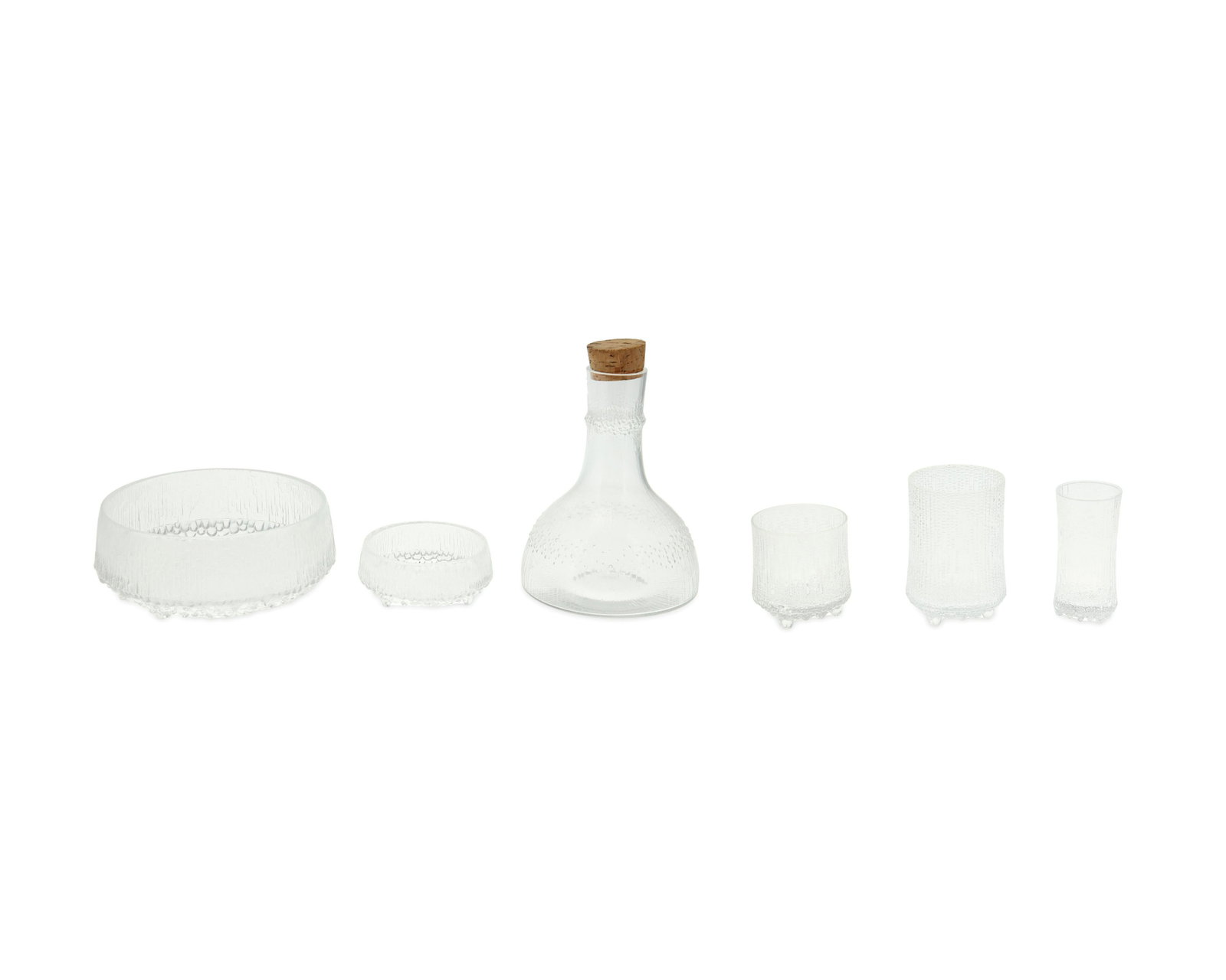 A group of "Ultima Thule" glassware by Tapio Wirkkala: Circa 1960s-70s Each with an ice and snow inspired motif, comprising a carafe with cork stopper (8.5" H x 6" Dia.), three highball glasses (5" H), six lowball/rocks glasses (3.5" H), three sparkling w
