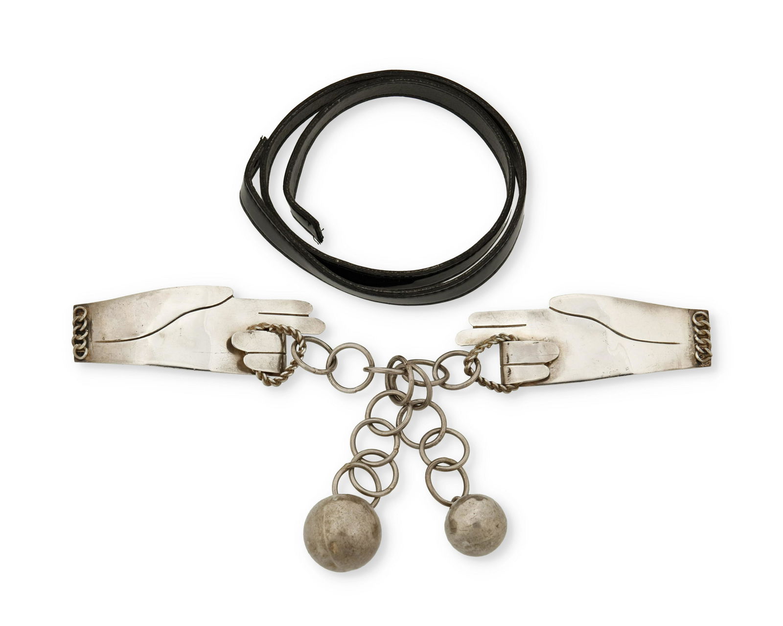 A Hubert Harmon silver hand belt buckle: 1944-1948; Taxco, Mexico Each stamped: Hubert Harmon / Sterling / Made in Mexico Designed as two hands pulling a silver chain suspending two metal spheres on a black patent strap 2 pieces Buckle:
