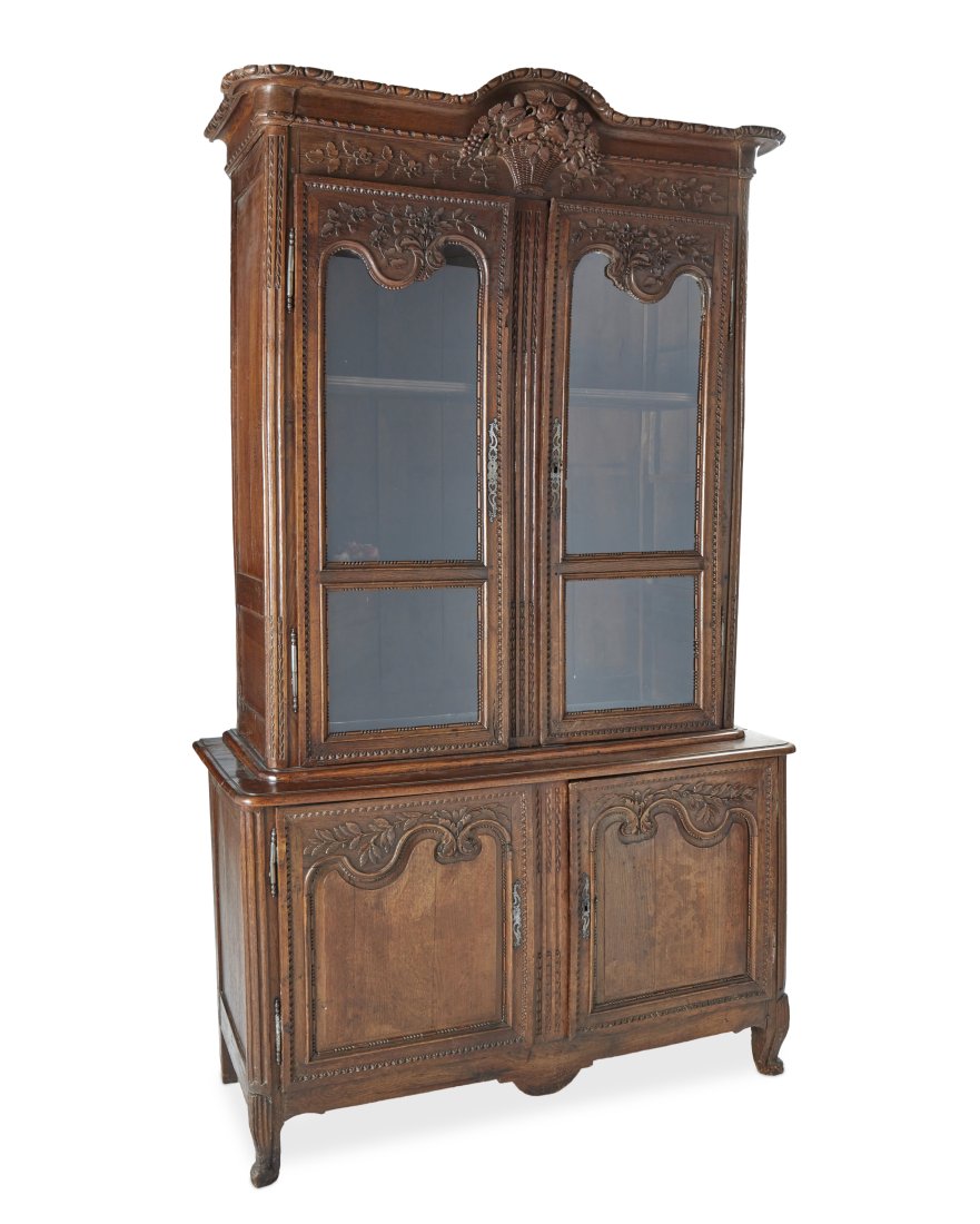 A French provincial vitrine cabinet: Late 18th/Early 19th Century With remnants of two paper export labels: Orrouy-Glaines The carved wood cabinet with a glazed, double-door vitrine surmounted by a floral basket crest and fitted with two