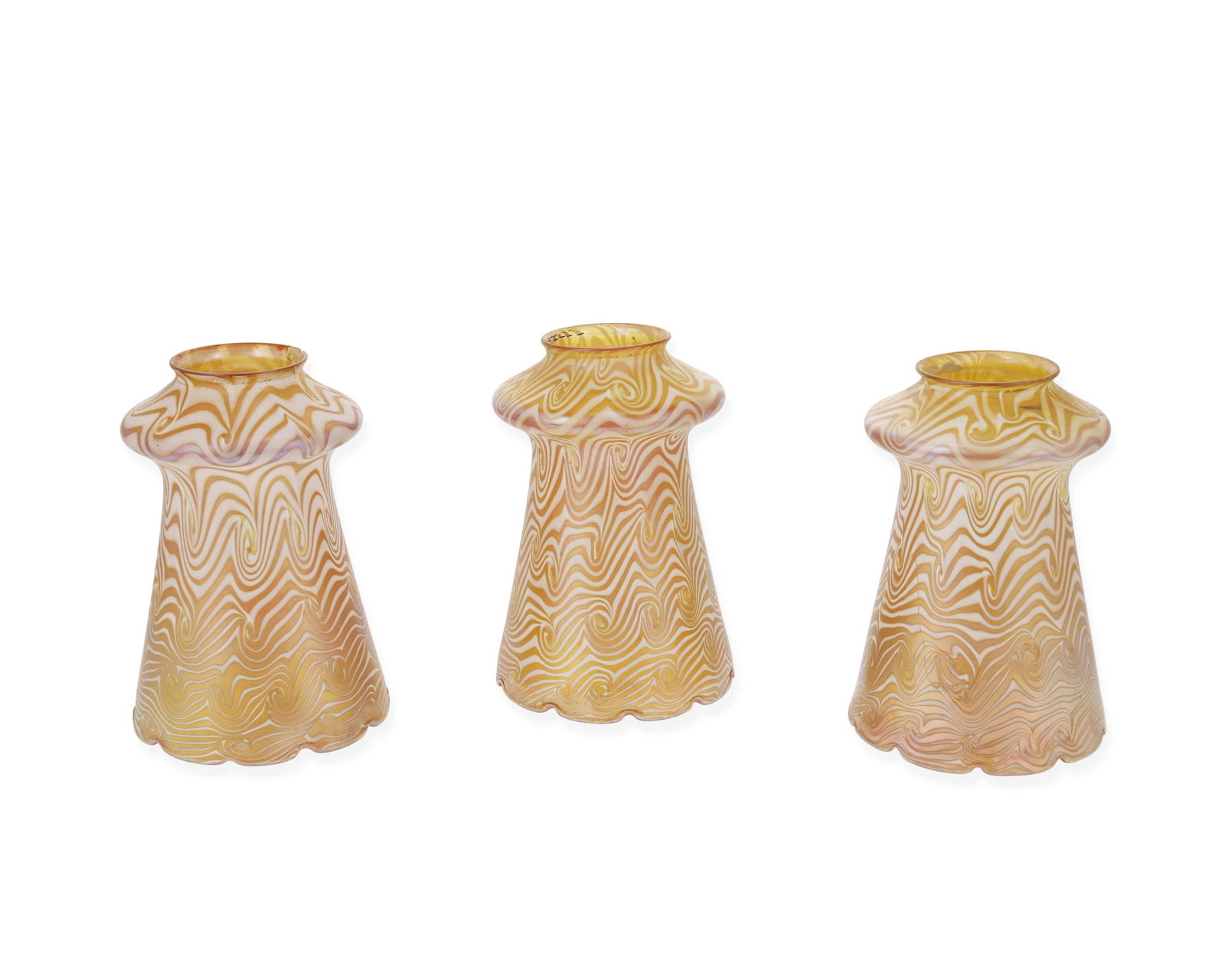 Three Quezal iridescent art glass shades: Early 20th century Each signed: Quezal Each bell-form gold iridescent glass shade with white swirl motif, 3 pieces Each: 6" H x 4.25" Dia.; fitter rim: 2.25" Dia.