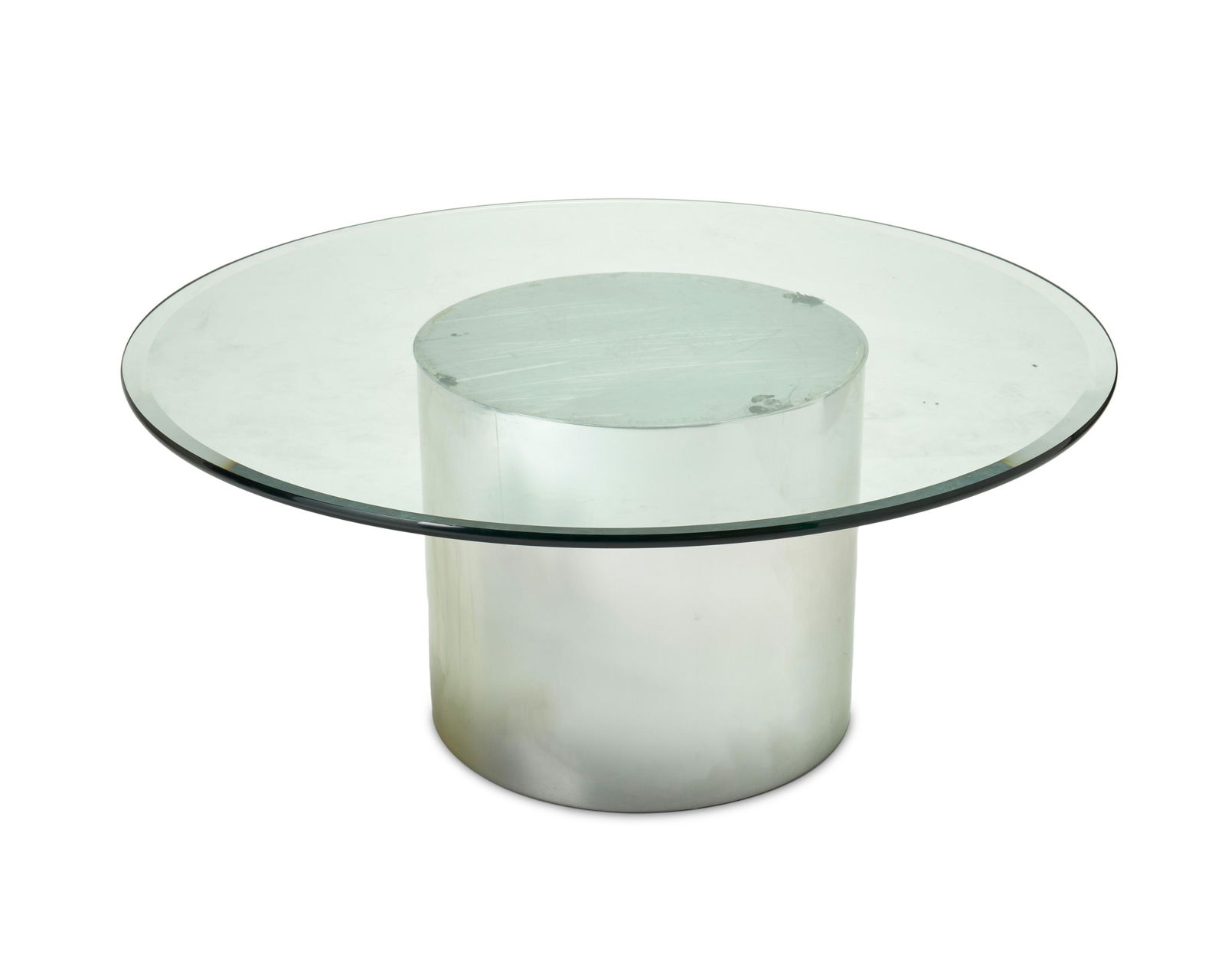 A Brueton-style polished chrome and glass cocktail table: Circa 1980s The contemporary table with a polished, cylindrical chrome base and a circular glass top 20.5" H x 48" Dia.