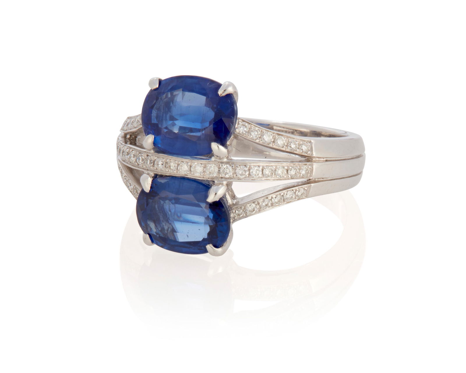 A sapphire and diamond ring: 18k white gold; Stamped: 18k / 750 / 08 Comprising of two oval mixed-cut sapphires each gauged at 8.8mm x 6.6mm x 3.7mm (and 3.9mm) each weighing approximately 1.70cts. and 1.80cts. further accented