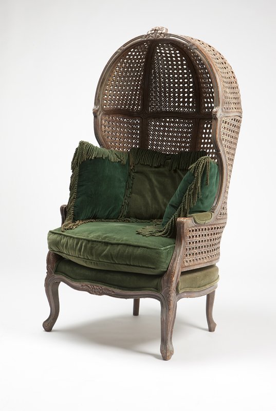 A Louis XV style carved wood and cane porter's ch: First half 20th century, the hooded, domed back surmounted by a floral crest and joined by padded scrolled arms to the serpentine padded seat, over a serpentine floral-carved apron raised on cabriole 