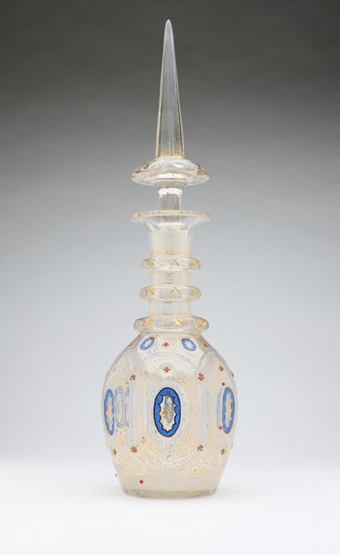 A Bohemian gilt and enameled clear glass decanter: 19th century, decorated with blue and gilt medallions, gilt tracery and ruby glass beads, with spire-shaped stopper, 21.25'' H x 6'' Dia., est:$1000/1500. Provenance: Private Collection, Glendale, CA