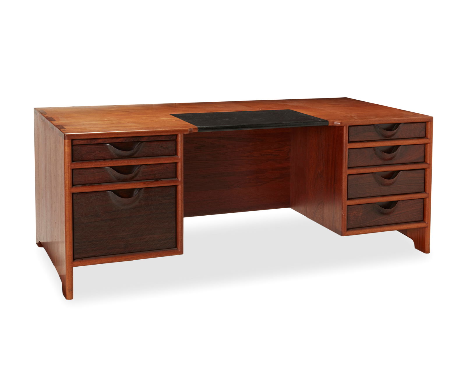 John Nyquist (1936-2018), A teak and rosewood desk, circa 1976, 28" H x 72" W x 33.25" D: John Nyquist (1936-2018)A teak and rosewood desk, circa 1976Designed 1975Marked with the artist's logo incised to bottom right drawerThe desk with inset leather top and seven drawers, each with carved