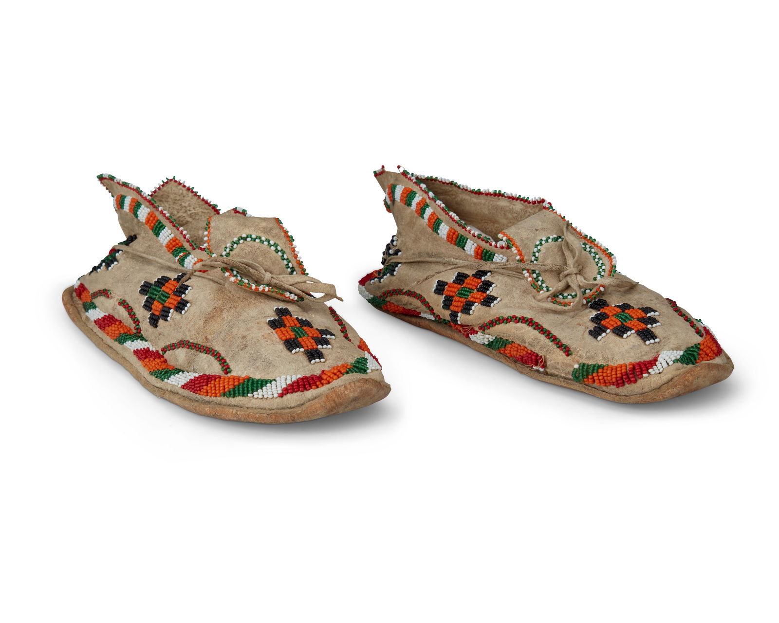 A pair of Plains beaded hide moccasins: A pair of Plains beaded hide moccasinsEarly/mid-20th centuryEach hide moccasin with geometric motifs in orange, white, green, black, and red beads to front and side edges, with decorative tongue and h