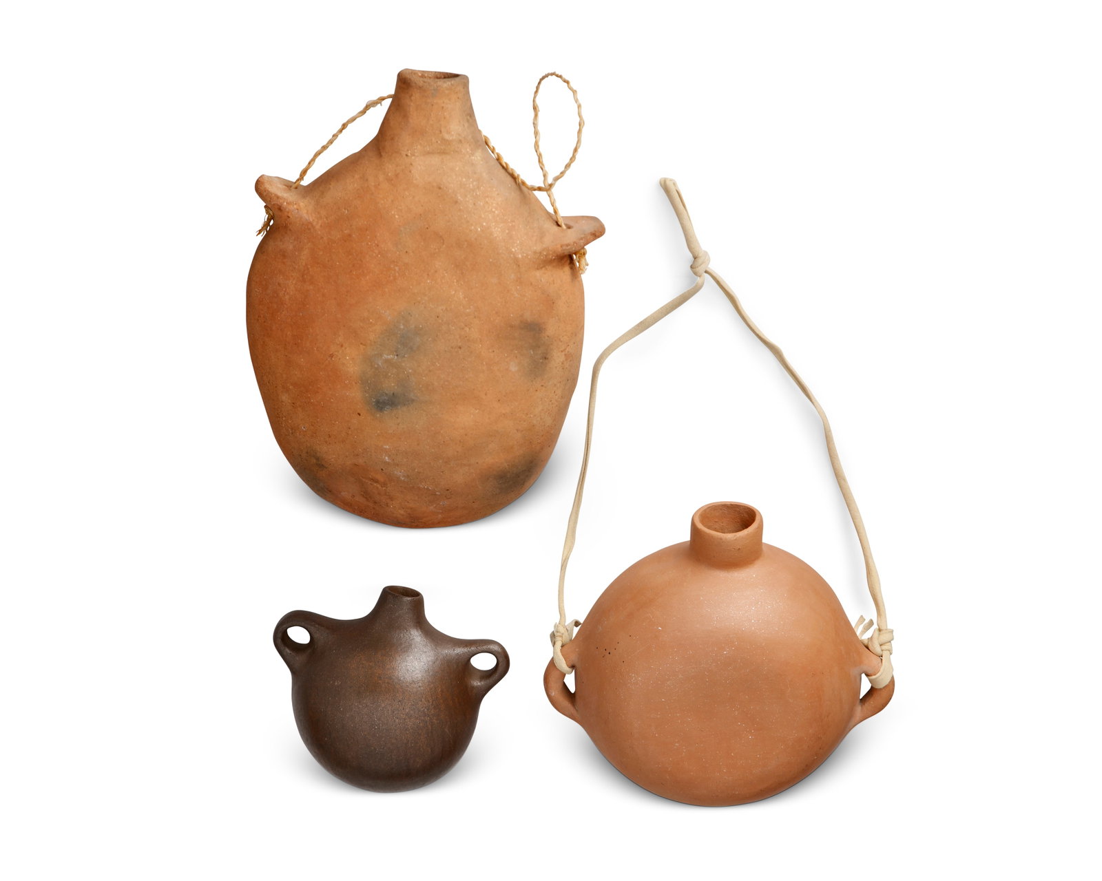 Three Puebloan micaceous pottery canteens: Three Puebloan micaceous pottery canteens 20th century; Southwestern United States Brown canteen incised: Romero; strapped canteen signed illegibly Comprising one large older canteen with twisted fibr