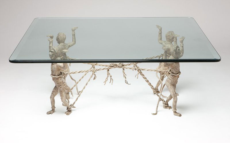 A painted cast bronze & glass monkey table: Late 20th century, apparently unsigned, the rectangular beveled glass top supported on a base composed of four figures of monkeys depicted walking away from each other in four directions with their ar