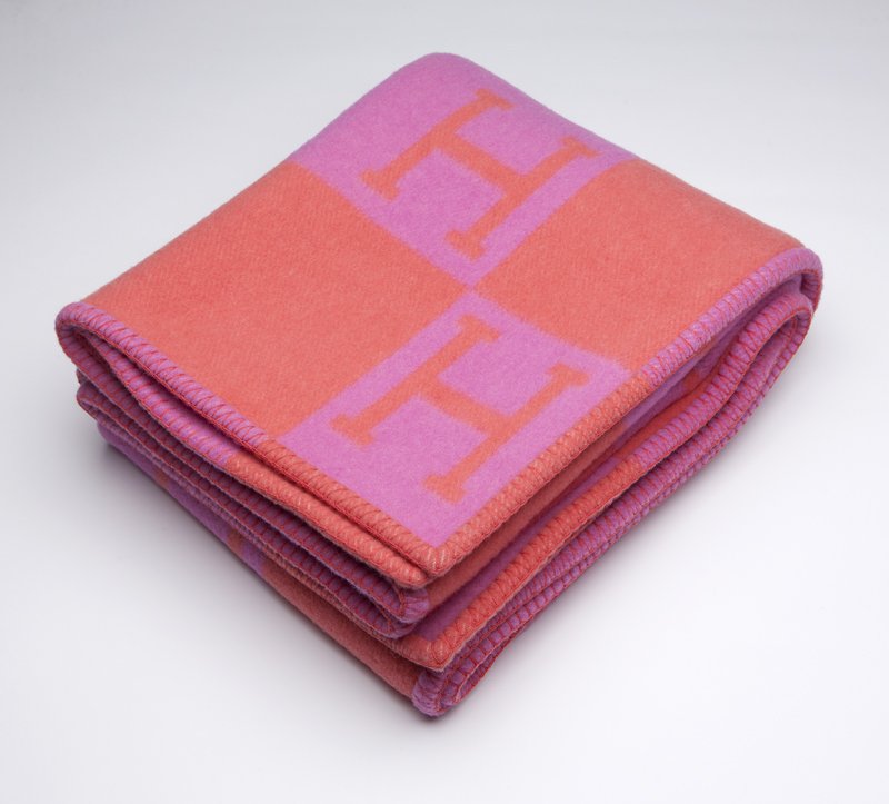 An Hermes 'Avalon' wool and cashmere blanket: Retains Hermes label, made in Scotland, in coral and pink with ''H'' pattern throughout and blanket-stitch edge, 68'' H x 52'' W, est:$400/600 Note: The 'Avalon' blanket currently retails at Hermes.co