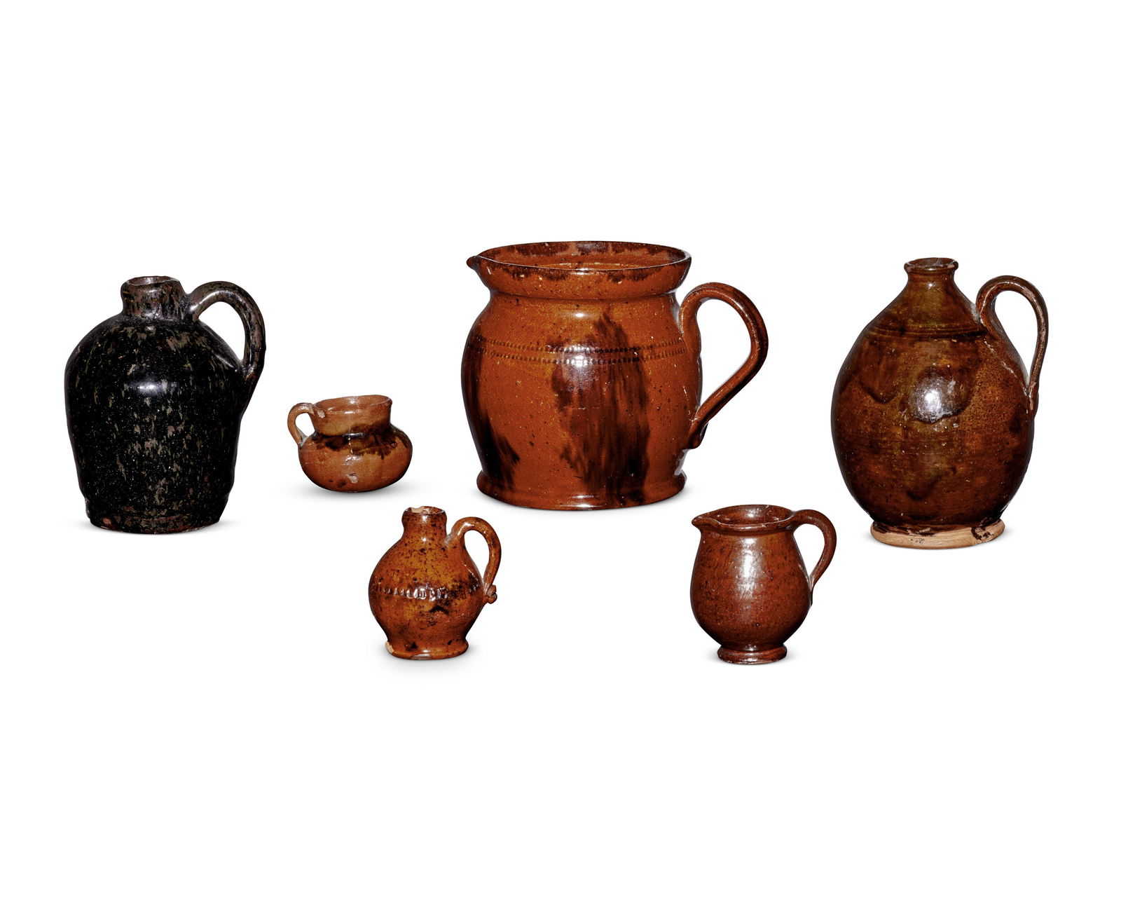 A group of Pennsylvania redware pottery vessels: A group of Pennsylvania redware pottery vessels18th/19th centuryEach unmarkedThe glazed earthenware group comprising a large handled pitcher with banded sgraffito details, a small handled pitcher, thr