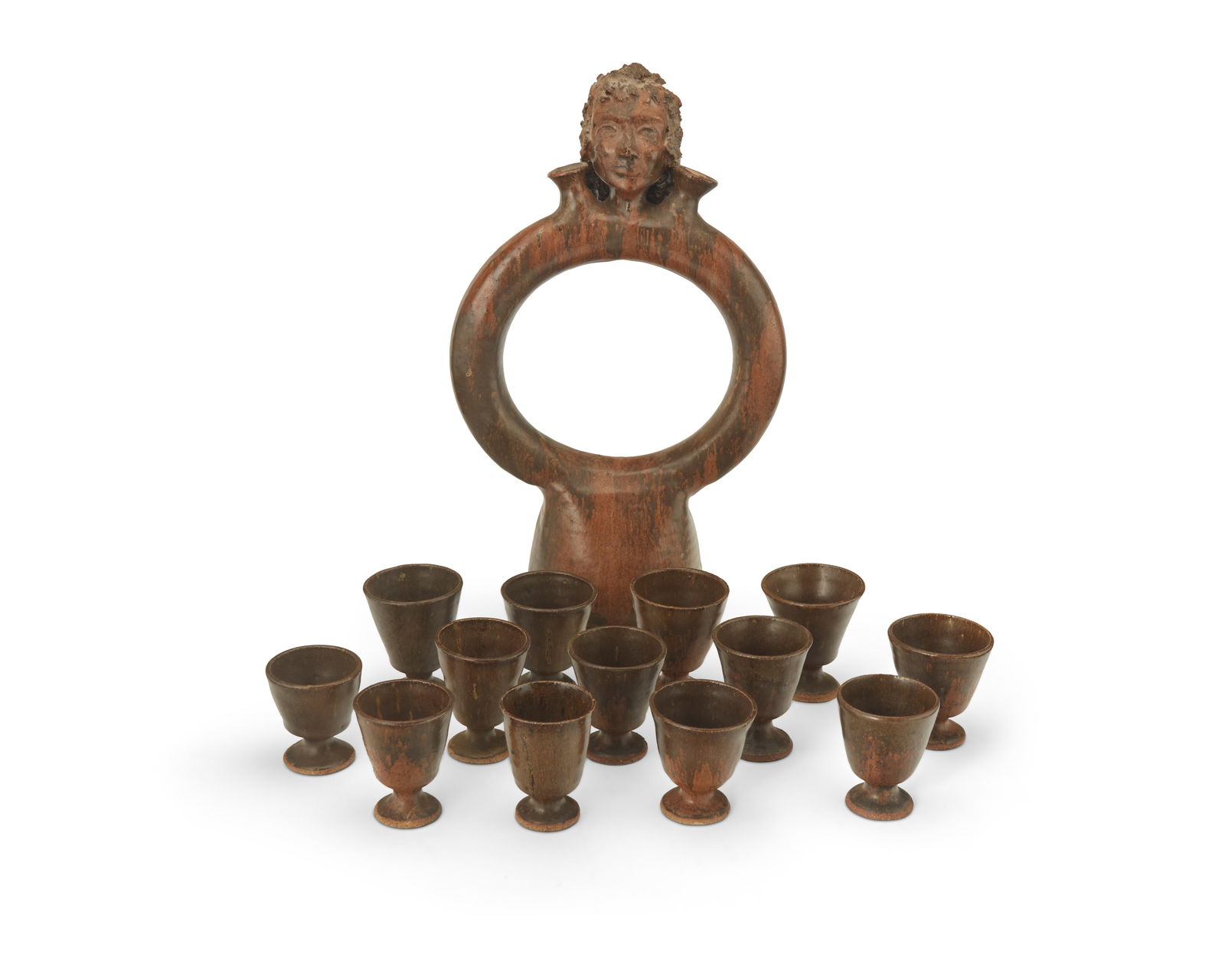 A glazed earthenware decanter and a group of goblets: A glazed earthenware decanter and a group of gobletsMid-20th centuryEach unmarkedThickly glazed in brown, the pottery group comprising a totemic decanter with figural head at the apex centering two fl