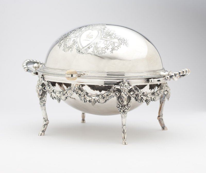 A Victorian silver-plated covered serving dish: Second half 19th century, Sheffield, mark of William Wheatcroft Harrison, the oval body with revolving cover enclosing a pierced line, on a double-handled stand raised on ram's mask-headed legs suspen
