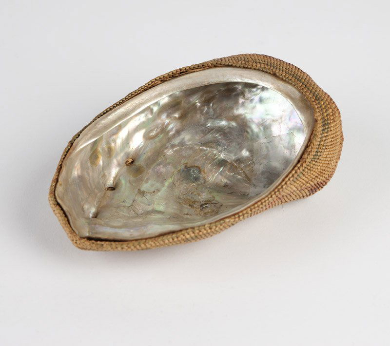 A Northwest Coast Nootka basket-covered shell: Late 19th / early 20th century woven over an abalone shell, the basket work polychrome-decorated in red, green and brown with a whale, a long boat with figures, and birds, 1.5'' H x 5'' W x 3.5'' D, e