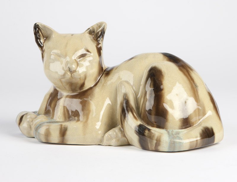 A Fulper ceramic 'Chinese Sleeping Cat' doorstop: First quarter 20th century, vertical oval 'Fulper' ink stamp to underside, depicted reclining with closed eyes, raised head and curled tail, covered in a tan, brown and blue flambe glaze, 5.25'' H x 9