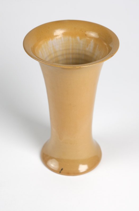 A Frederick H. Rhead Santa Barbara pottery vase: 1914 - 1917, with impressed logo of a potter at his wheel (Frederick Hurten Rhead 1880 - 1942), the flared rim extending to a tapering cylindrical body on a spreading foot, covered with a butterscotch