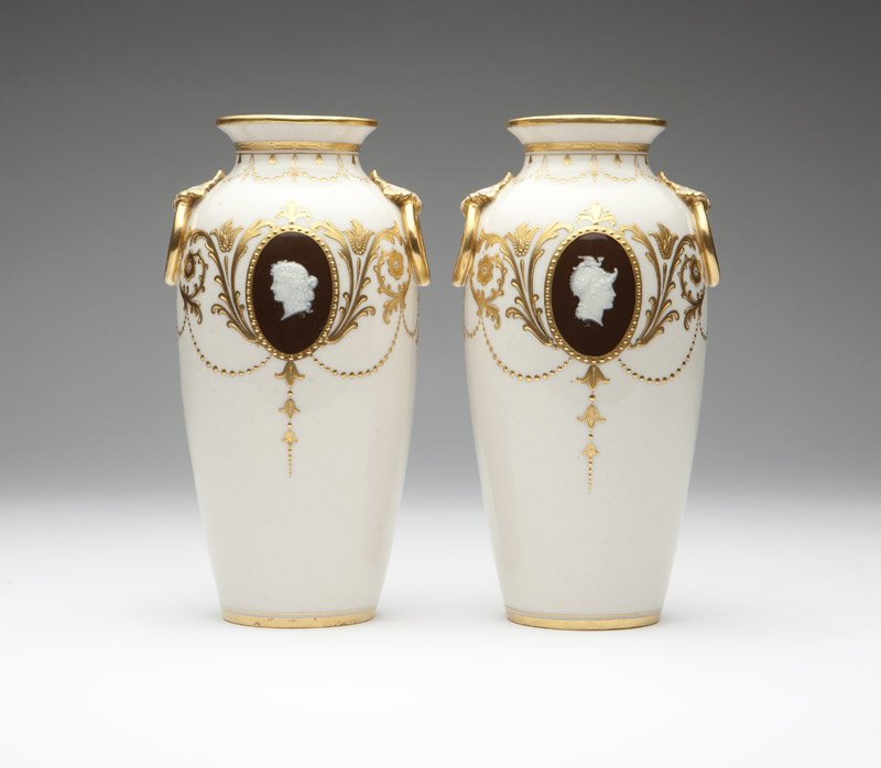 A pair Minton ivory-ground porcelain cameo vases: Circa 1900, each with gilt ''Mintons England'' crown and globe mark and faintly incised numbers, each baluster-form with gilt foliate scroll and garland decoration, each centering on one side a brown 
